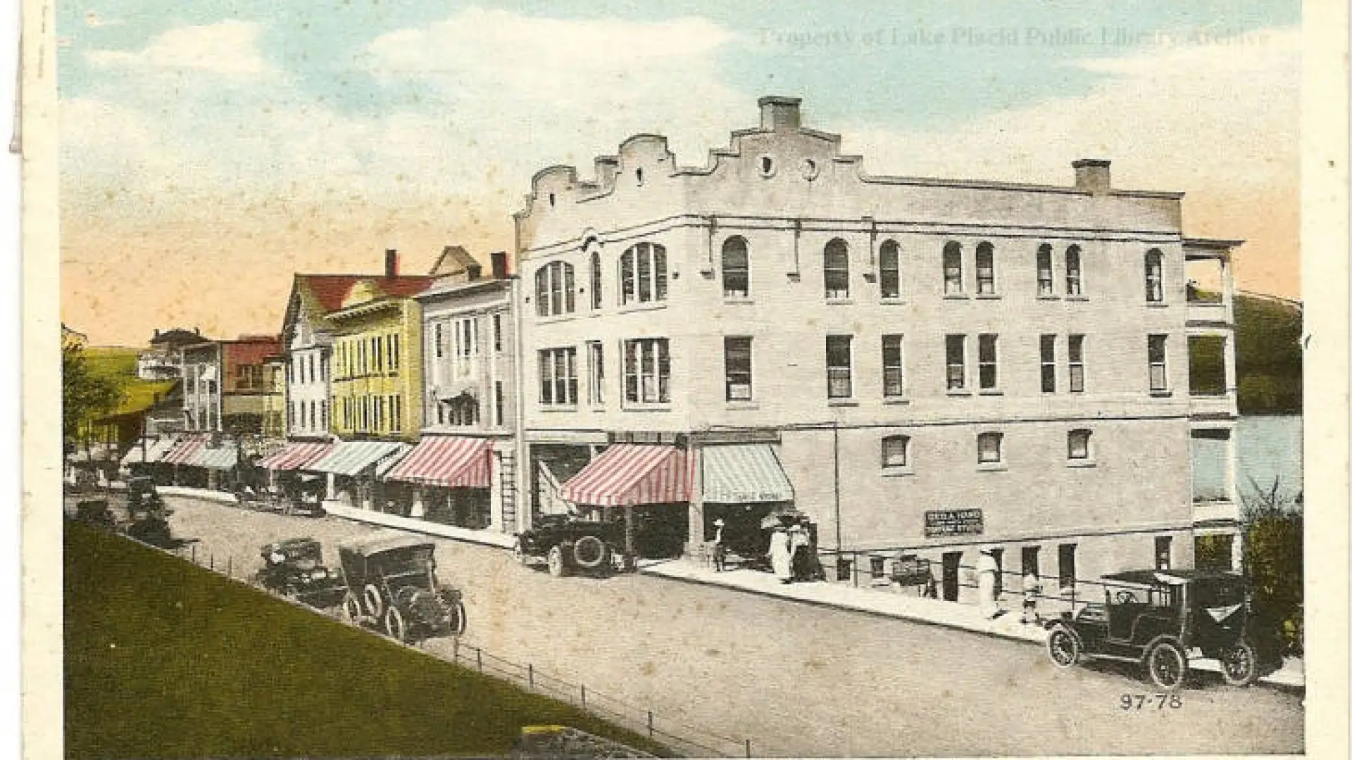 Vintage postcard of a row of buildings in Lake Placid, with early autos on the street. Image courtesy Lake Placid Public Library.