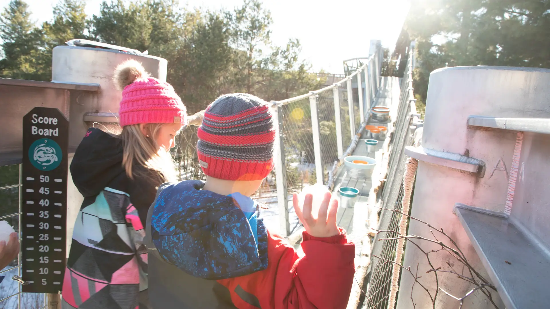 Two children play a game throwing snowballs into buckets set up on a suspended walkway on the Wild Center's Wild Walk
