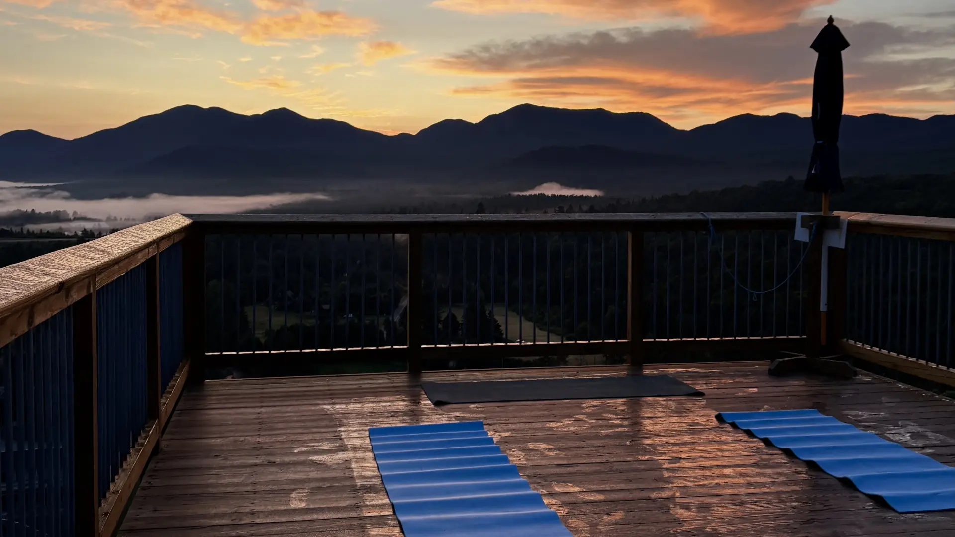 Two blue yoga mats on wooden deck with sunrise view on cloudy morning