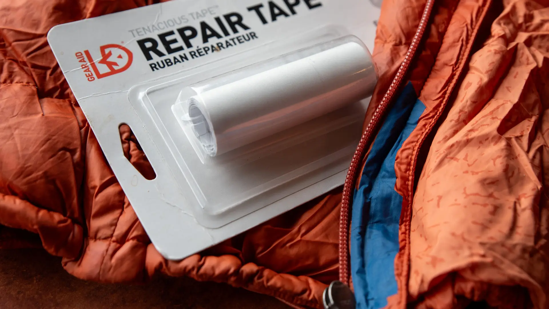 Package of repair tape sitting atop on orange technical wear jacket