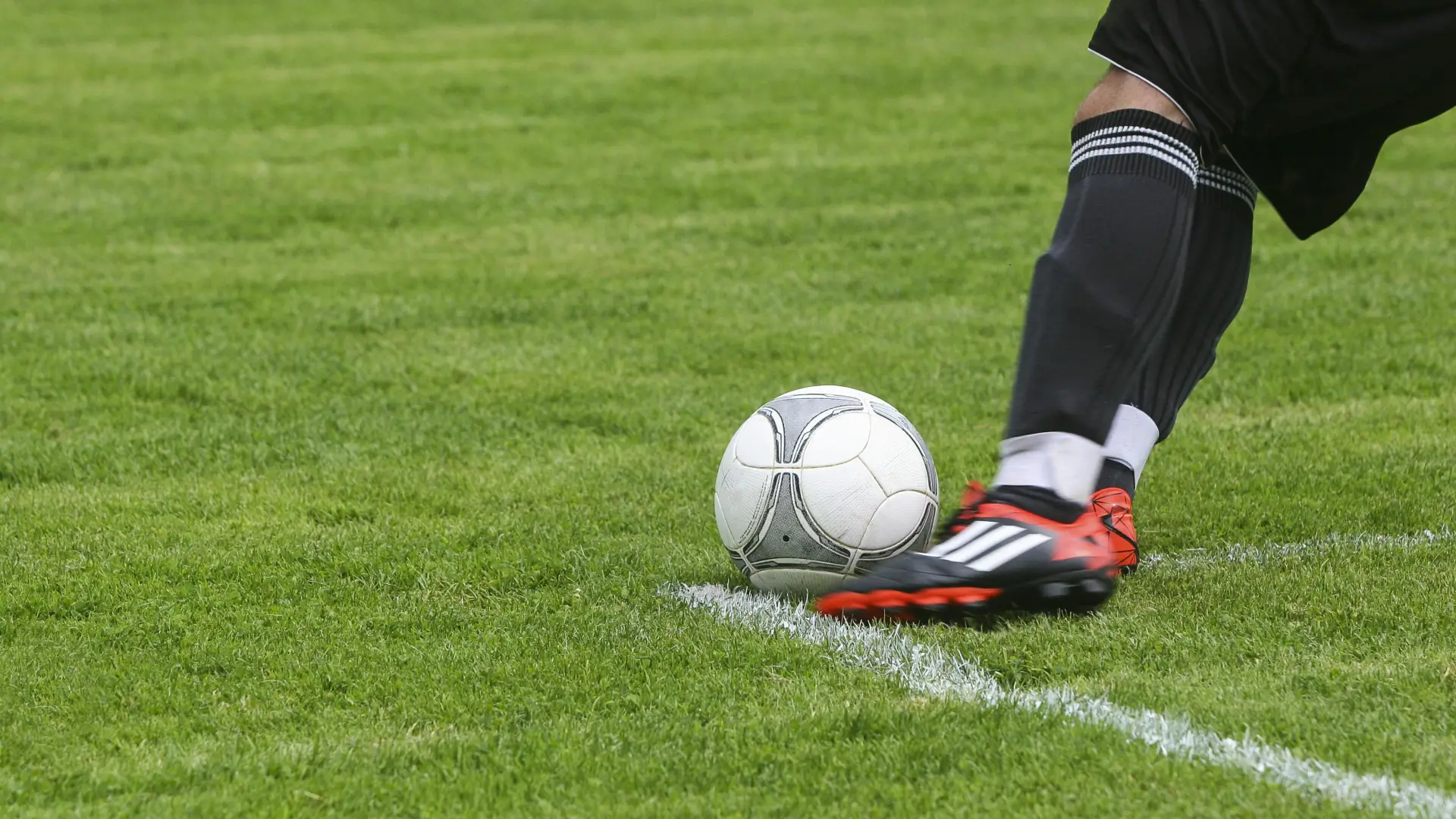 Cleated foot seen kicking a soccer ball on a green field with white lines
