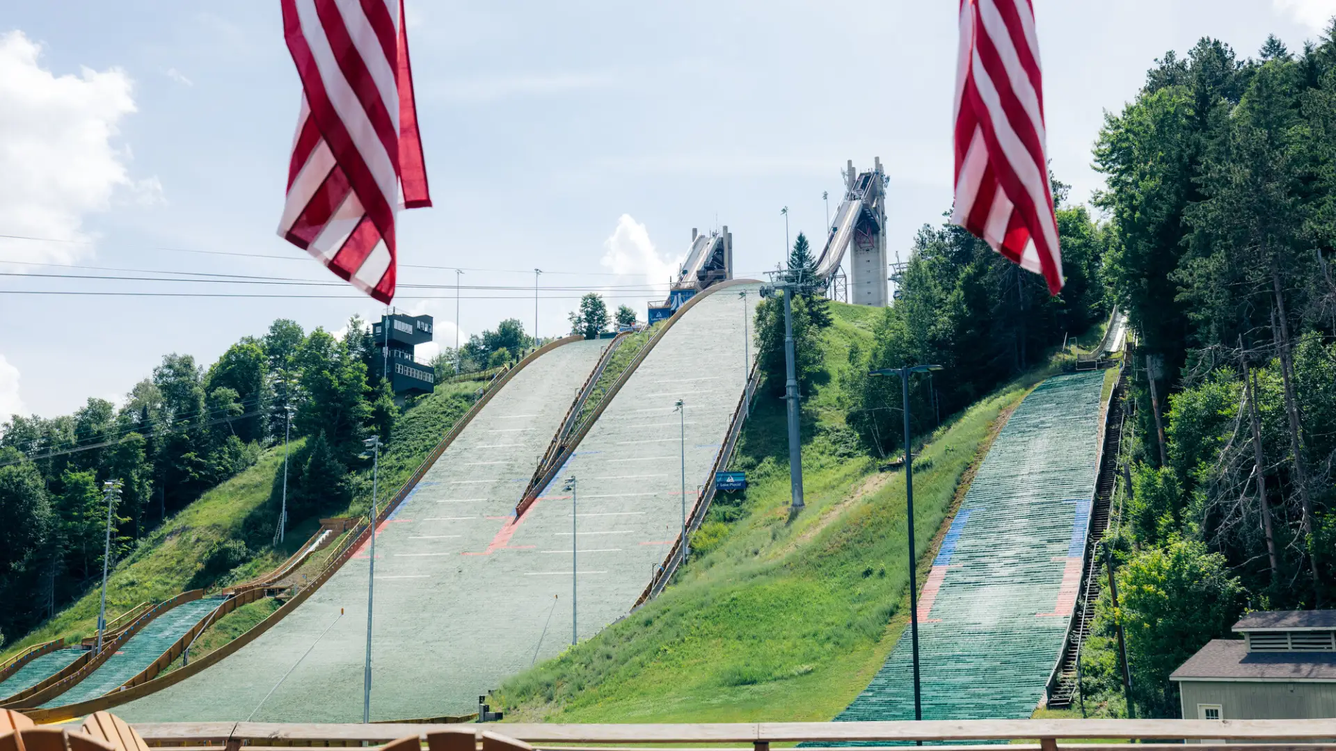 Looking up at the landing hills of the Lake Placid Ski Jumping Complex, framed by two American flags in the foreground.