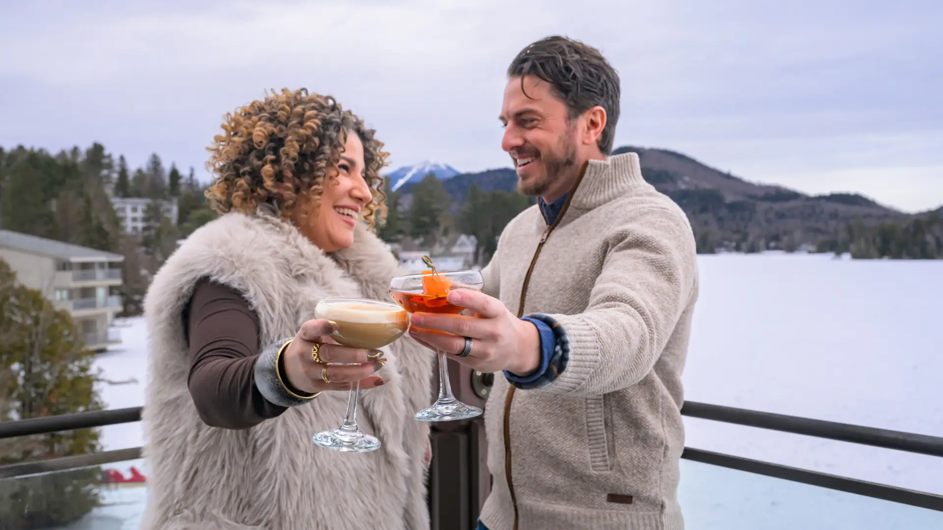 A man and woman cheers drinks on a snowy patio.