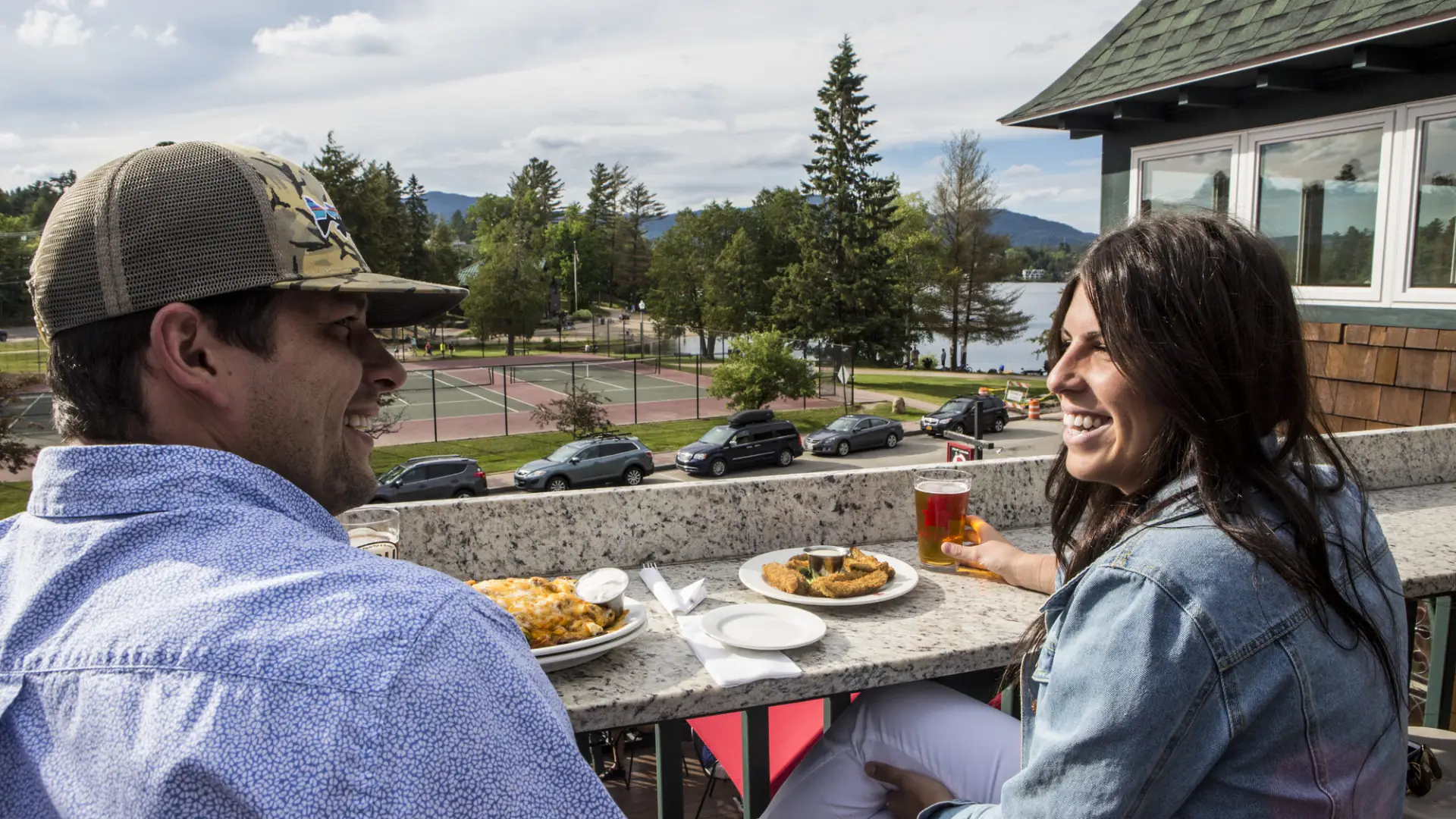 A couple smiles as they enjoy a meal on an outdoor deck.
