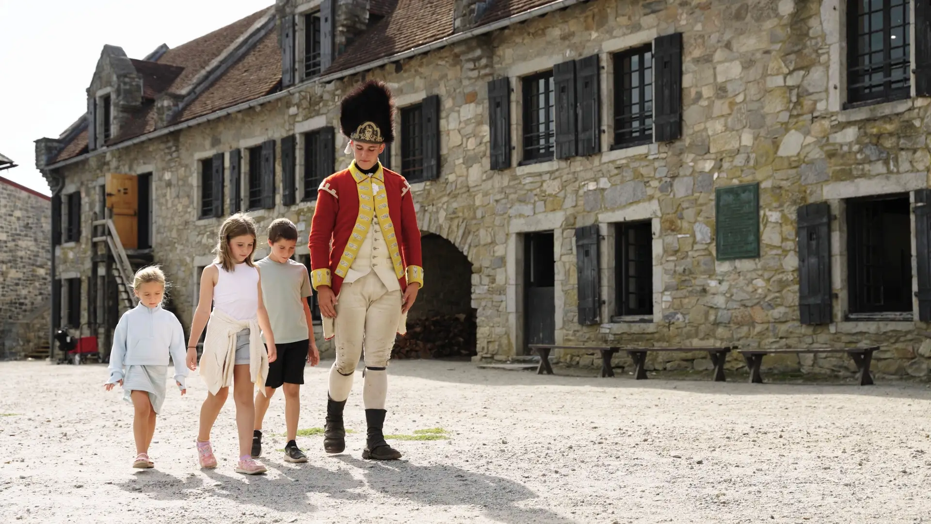 A young man dressed as a British soldier walks the cobblestone looking at shadows with a couple of kids