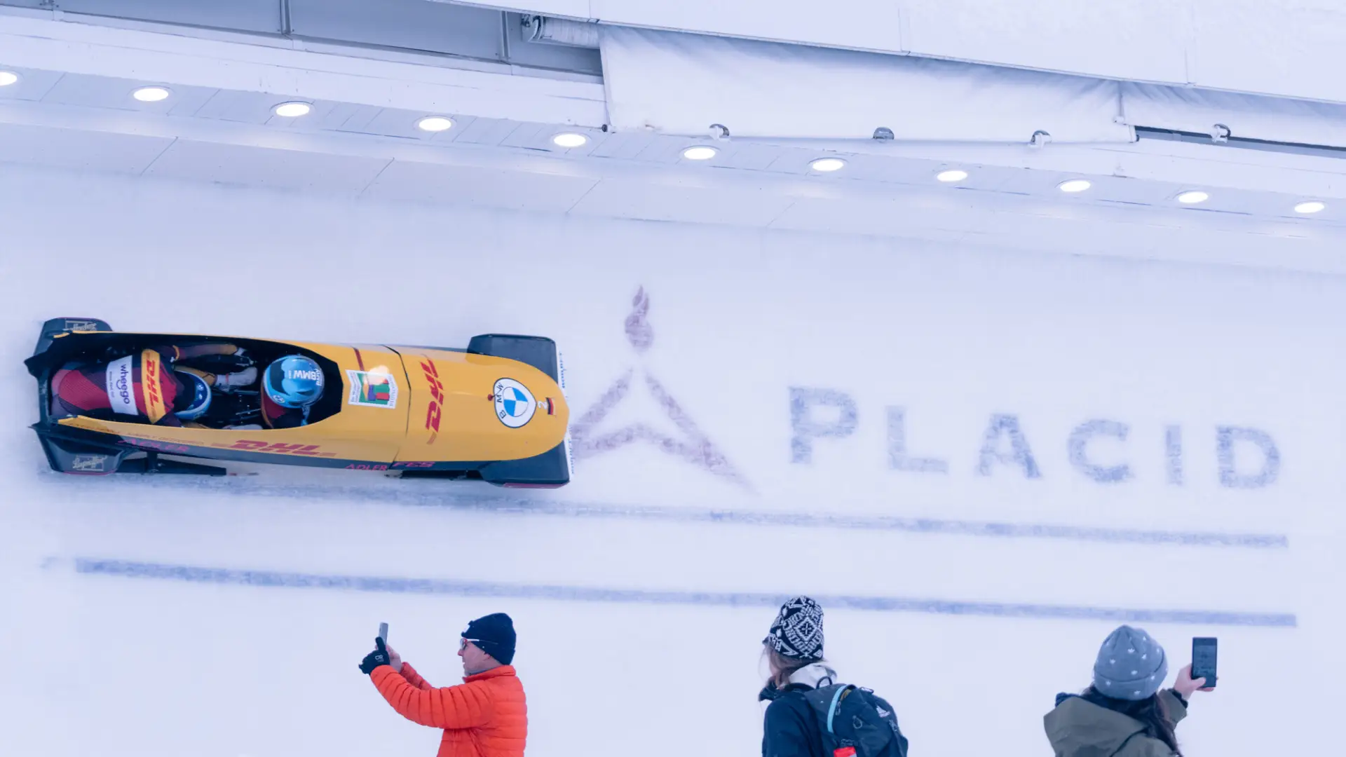 Spectators watching and taking photos of a Lake Placid bobsledding event.
