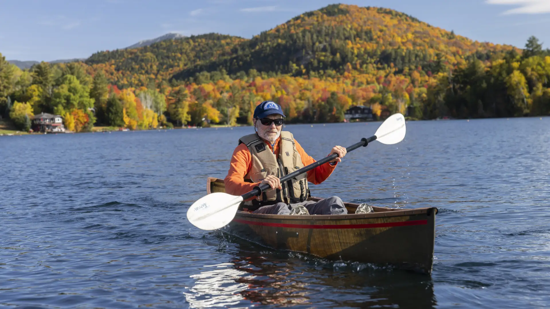 A man paddles on a lake surrounded by fall colors.