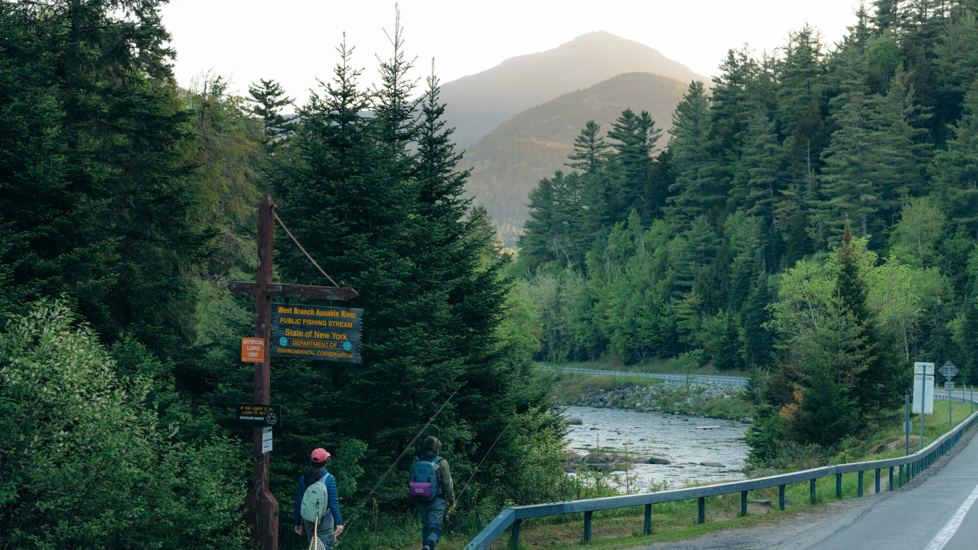 Two fly fishers walk towards a roadside river