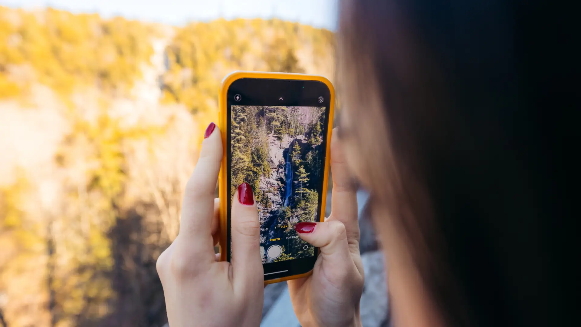 A woman takes a picture of a waterfall.