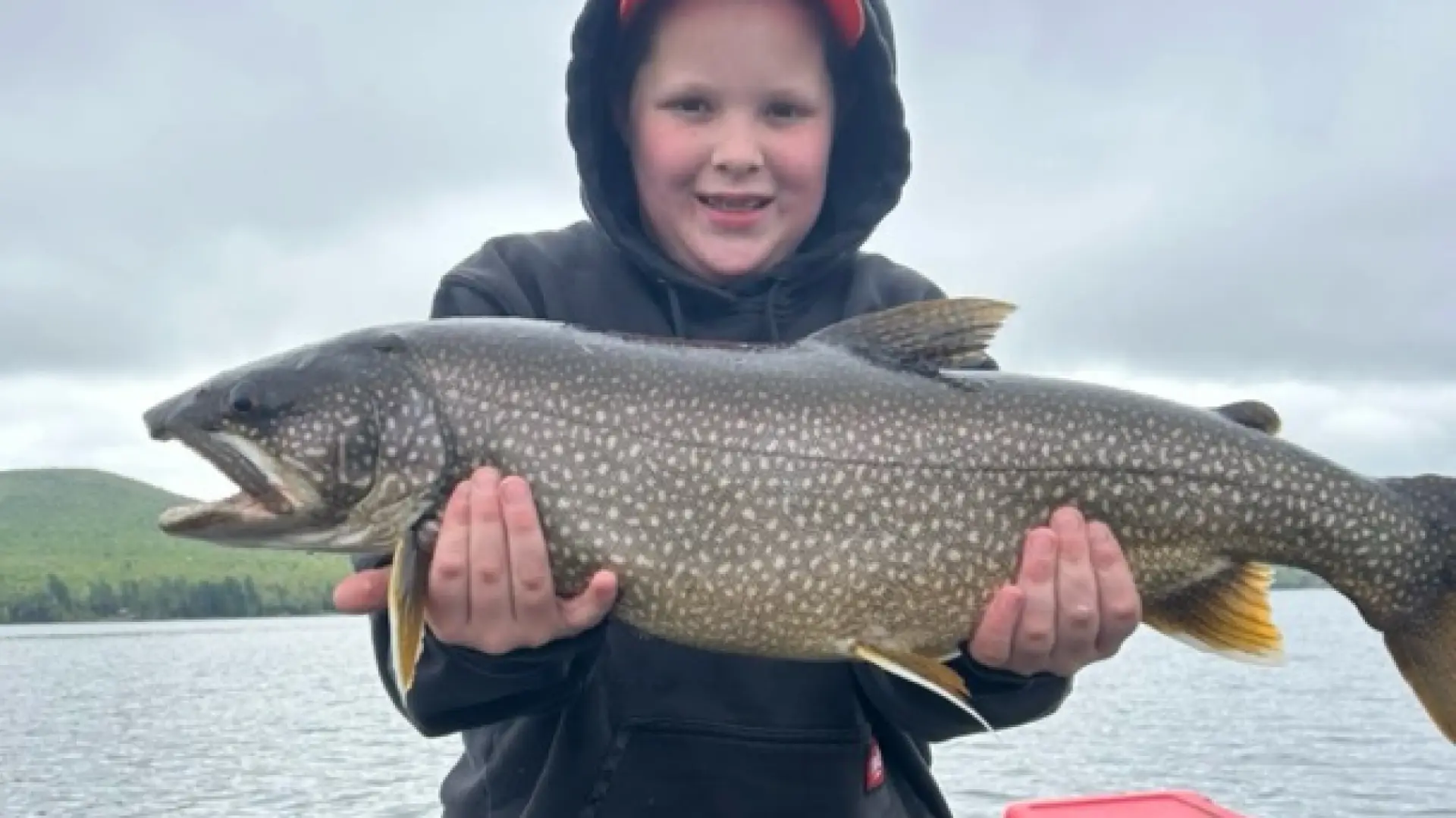 A smiling kid standing on a boat holding a large fish.