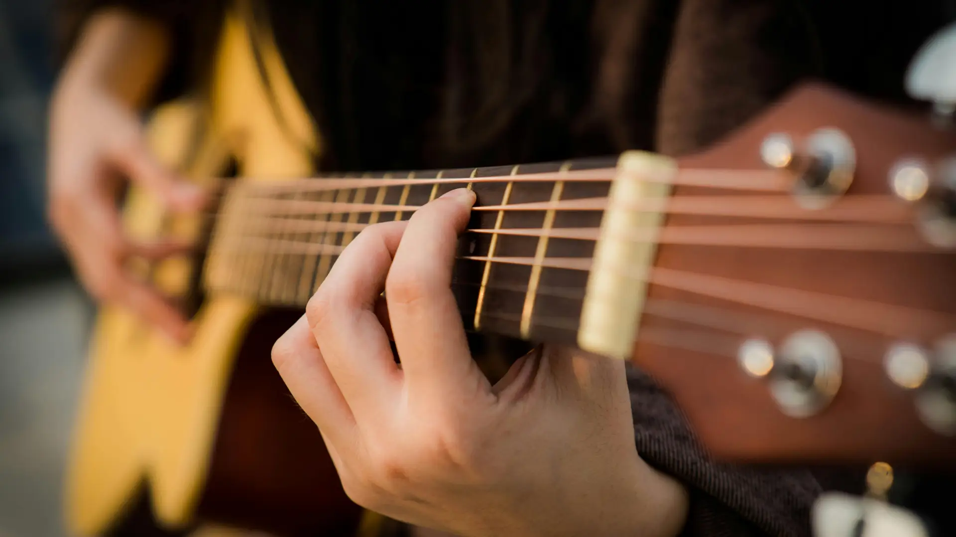 Stock image of guitar being played by person wearing black long sleeve shirt, holding chord on neck of guitar
