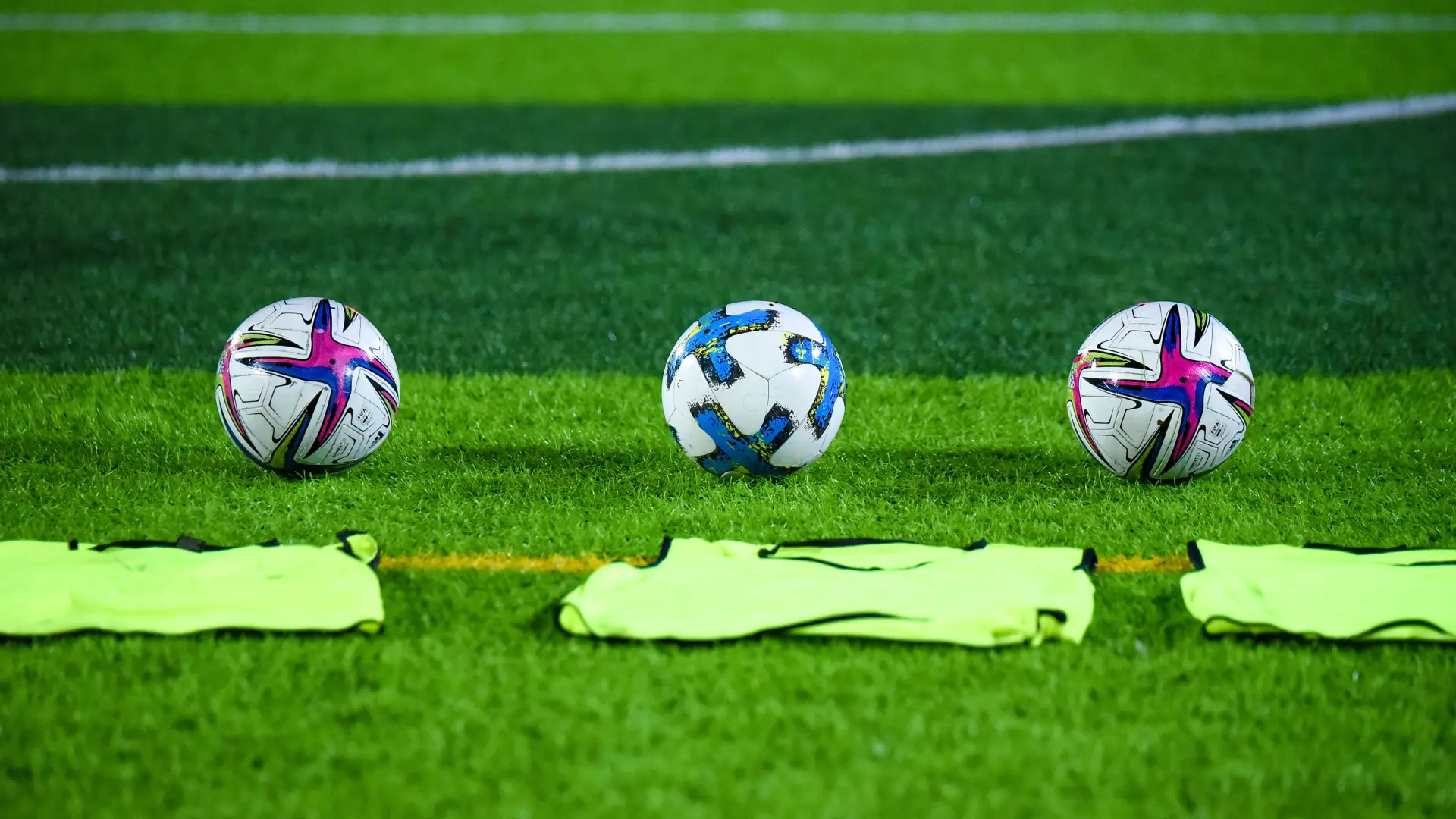 Three soccer balls on green soccer field with green pinnies laying on the ground in front of them