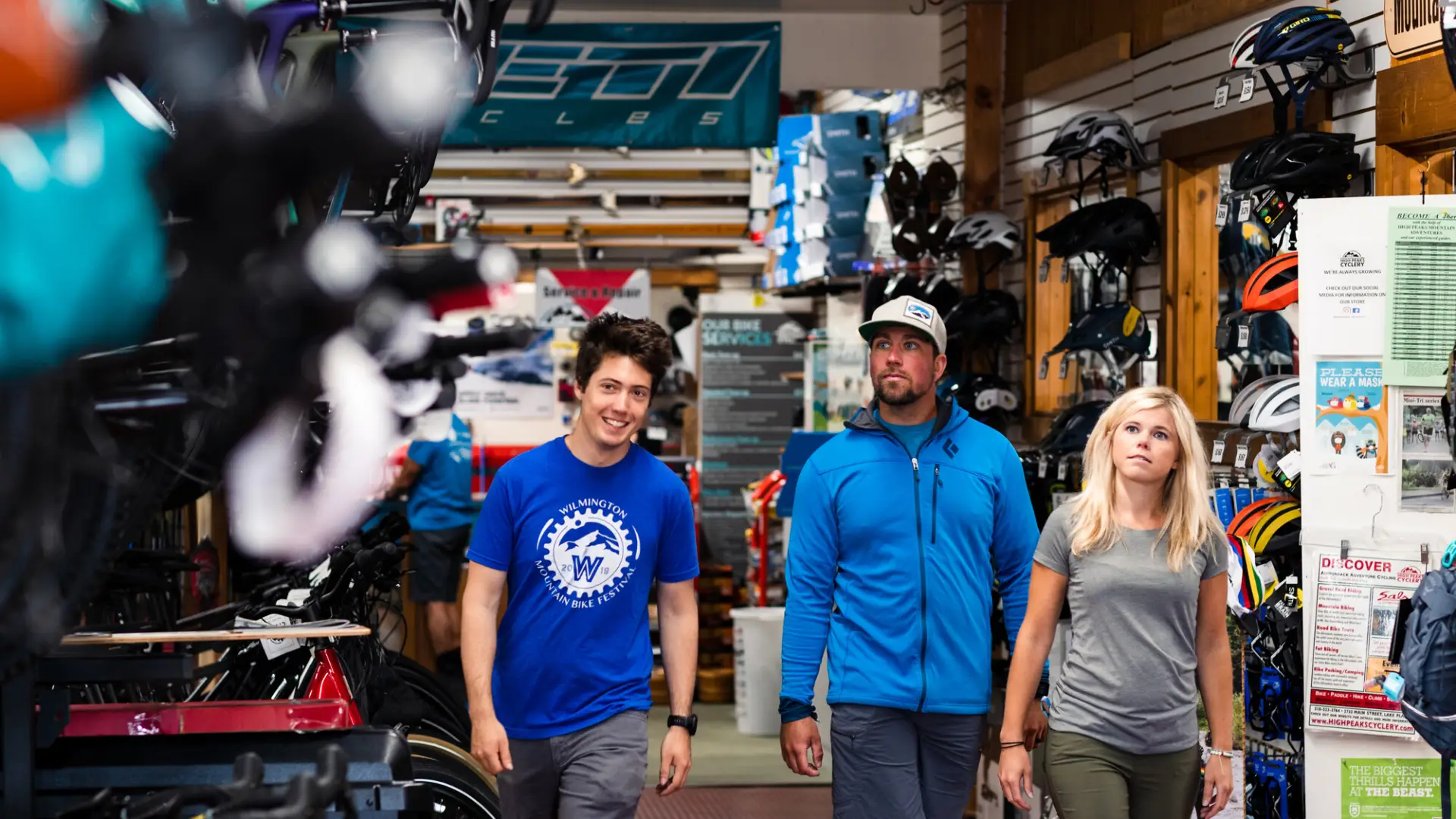 A bike shop employee leads a man and a woman to a display of bikes in a crowded shop.