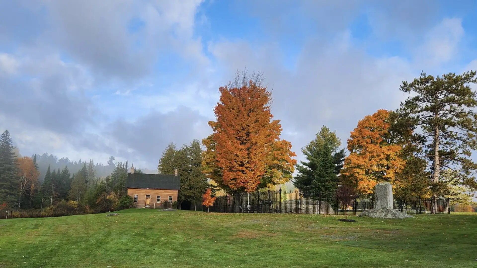 Abolitionist, John Brown's house sits on a grassy lawn, surrounded by fall foliage and a stone monument.