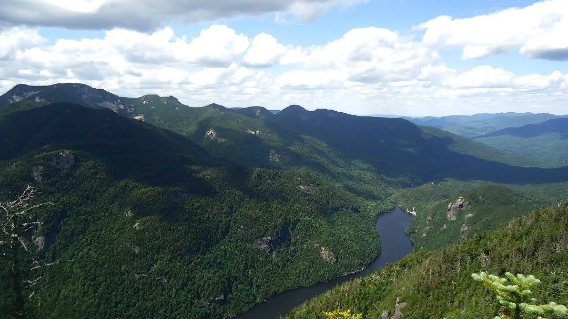 A long lake stretches out below High Peaks of green under a blue sky.