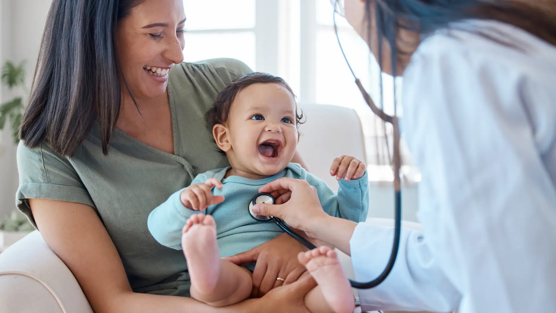 A woman holds a baby as a doctor listens to her heartbeat.