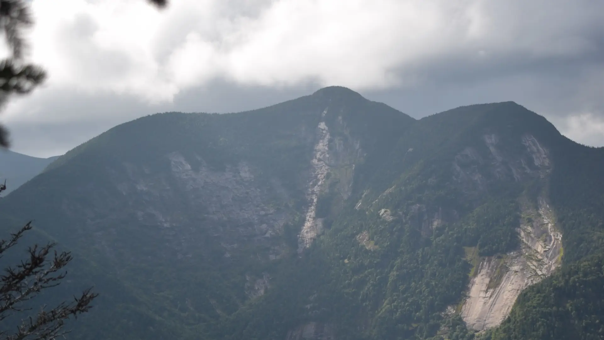 A through-the-trees view of a tall, three-peaked mountain