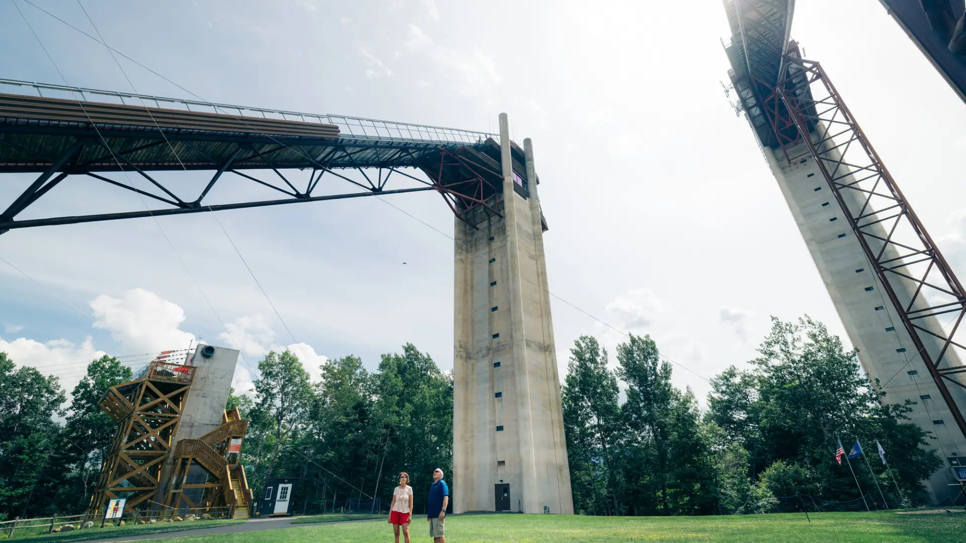 Senior couple stands on grass at the base between two towering ski jumps