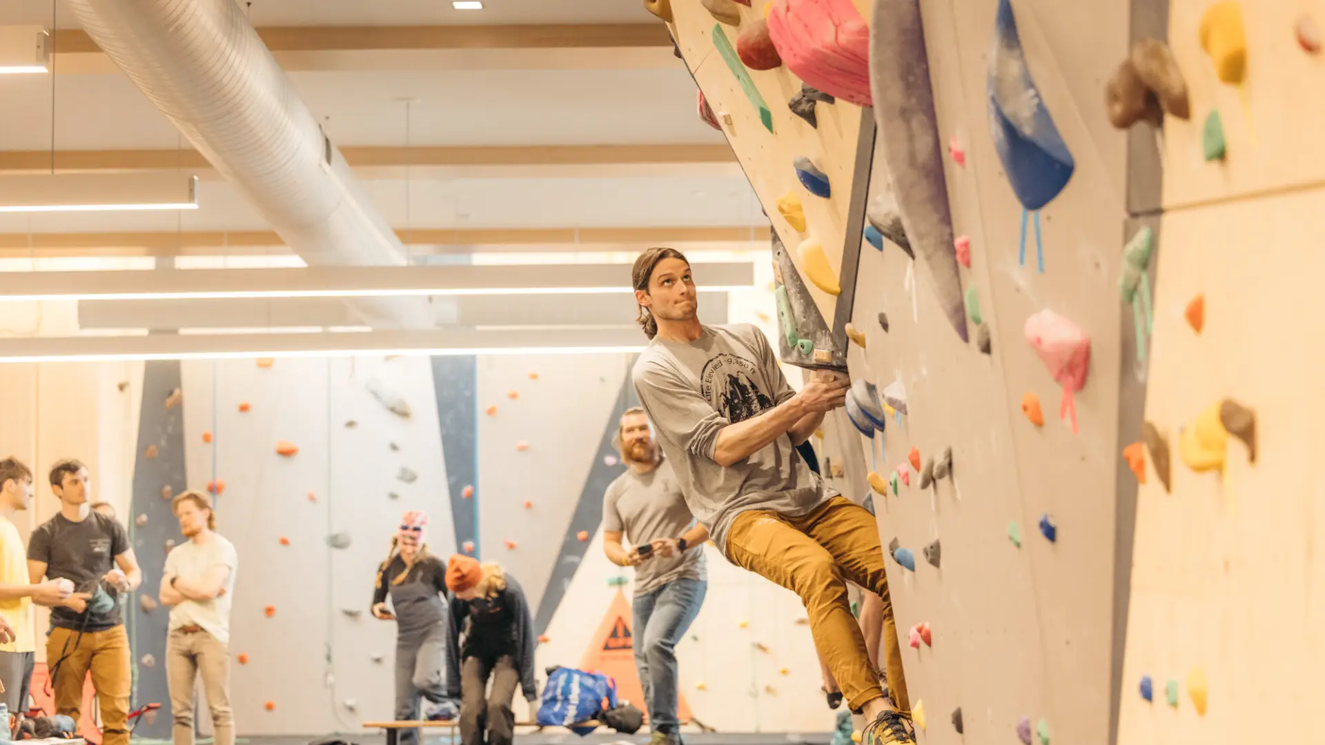 A man focuses intently while bouldering on a steep, multi-angled indoor climbing wall.