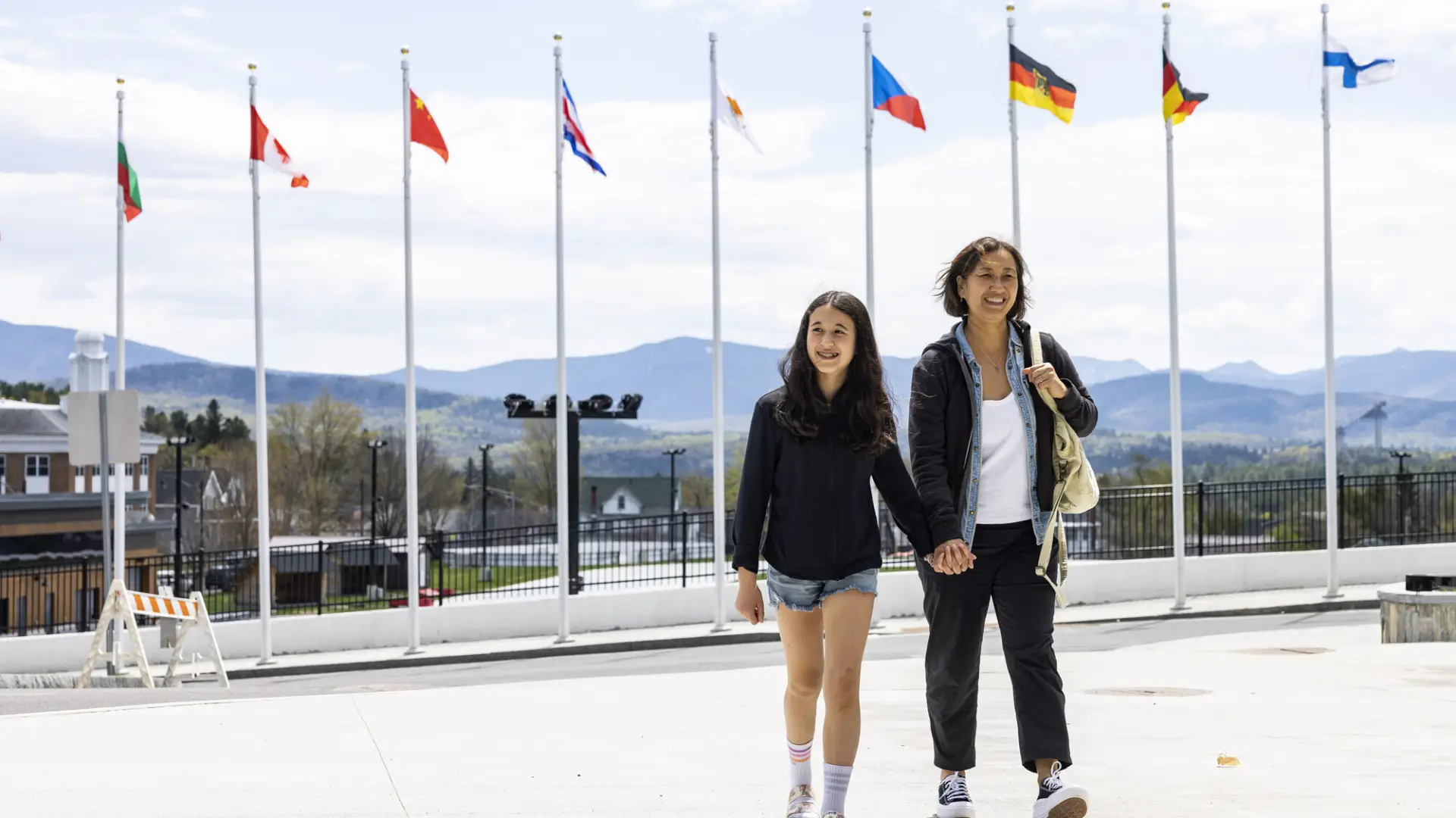A woman and her daughter walk in front of olympic flags. 