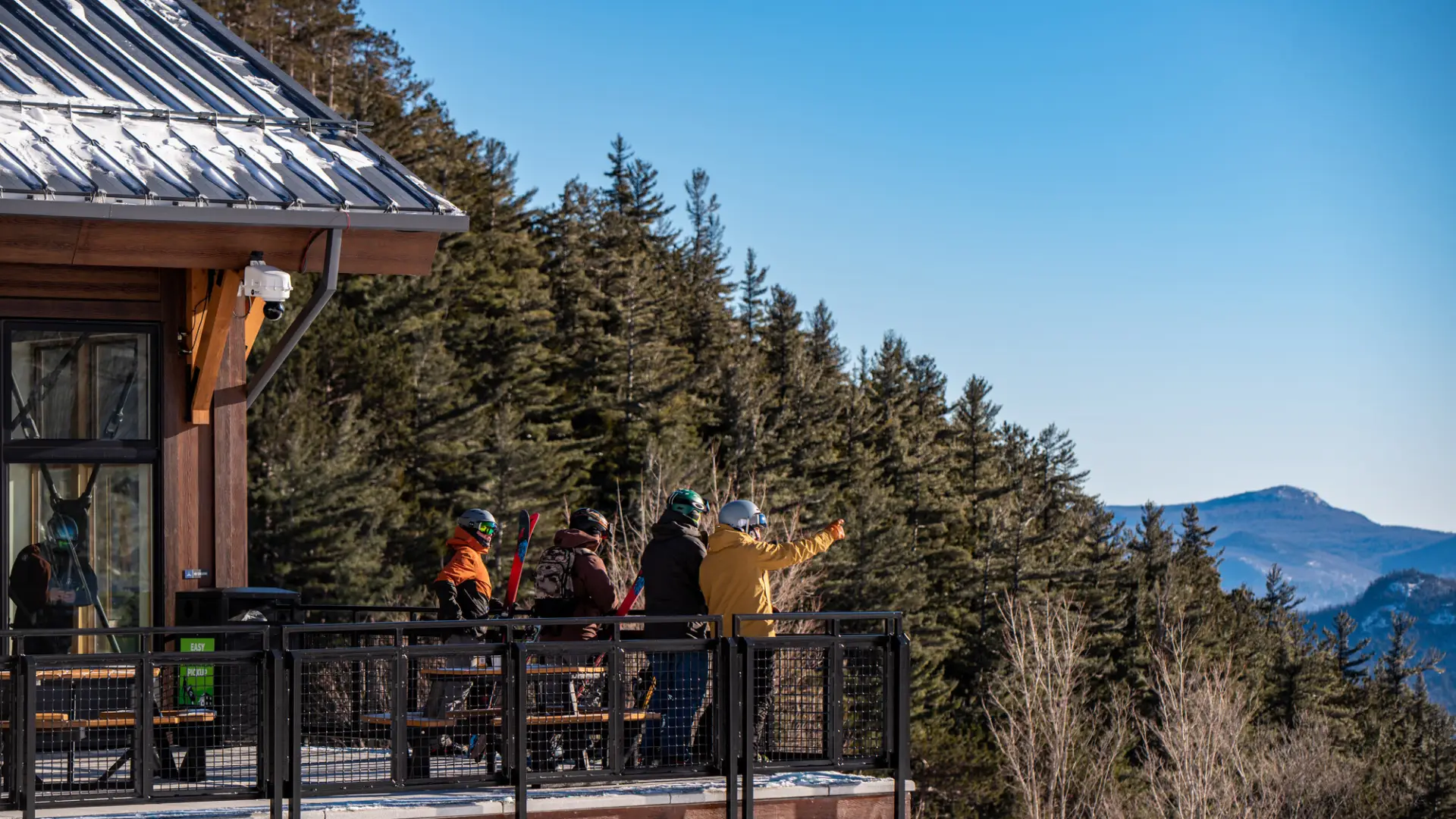 A group of skiers stand on the deck of a mountain lodge.