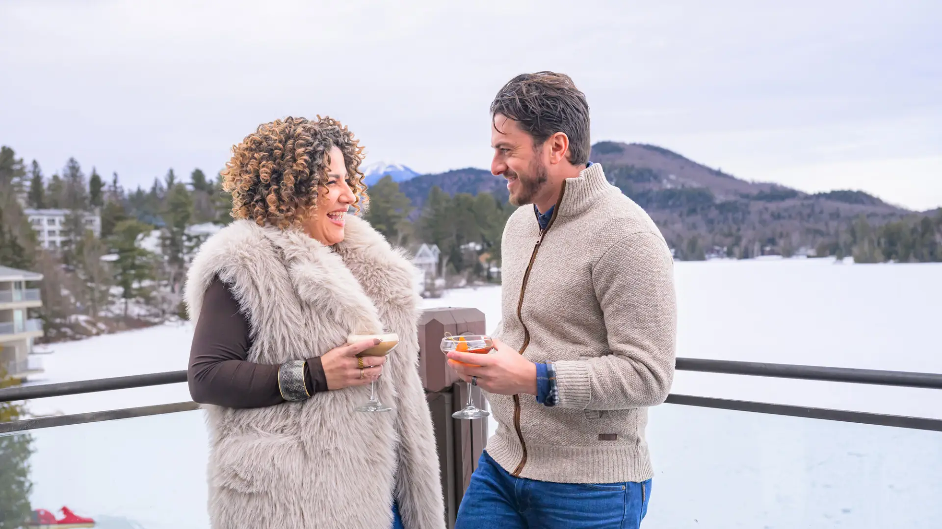 A couple standing on the patio at Top of the Park with cocktails and winter scenery behind them.