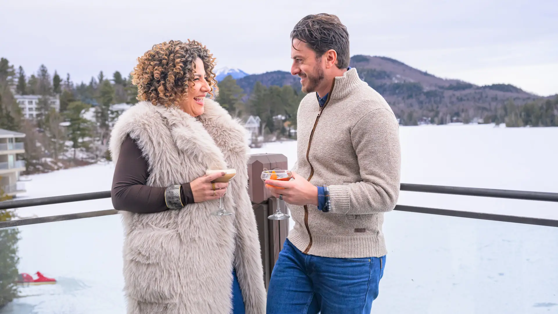 A couple standing on the patio at Top of the Park with cocktails and winter scenery behind them.