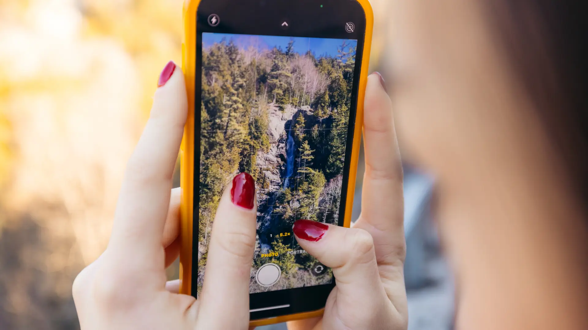 A woman takes a picture of a spring waterfall.