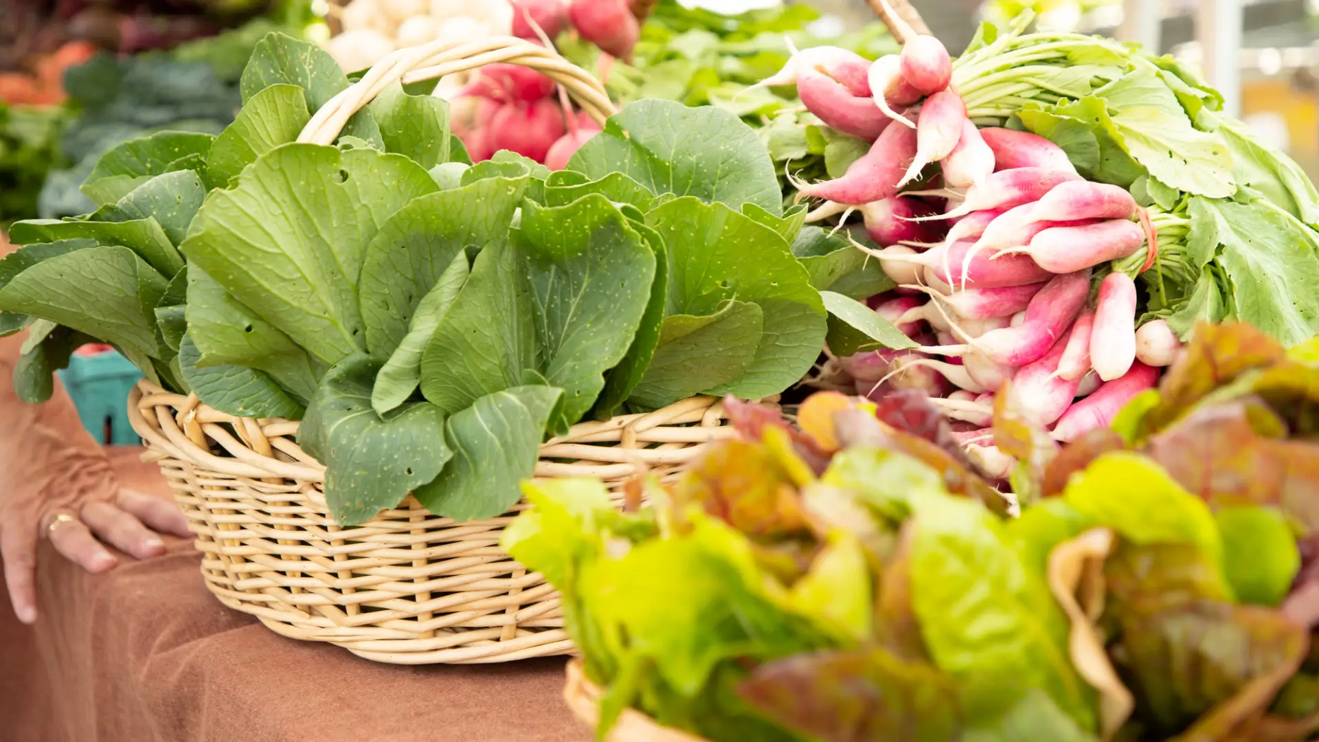 Baskets of greens and radishes on table at farmers' market