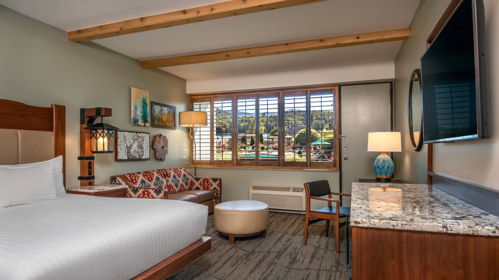 Hotel room with wooden ceiling beams, large bed with white bedspread, and seating area with patterned and leather couch