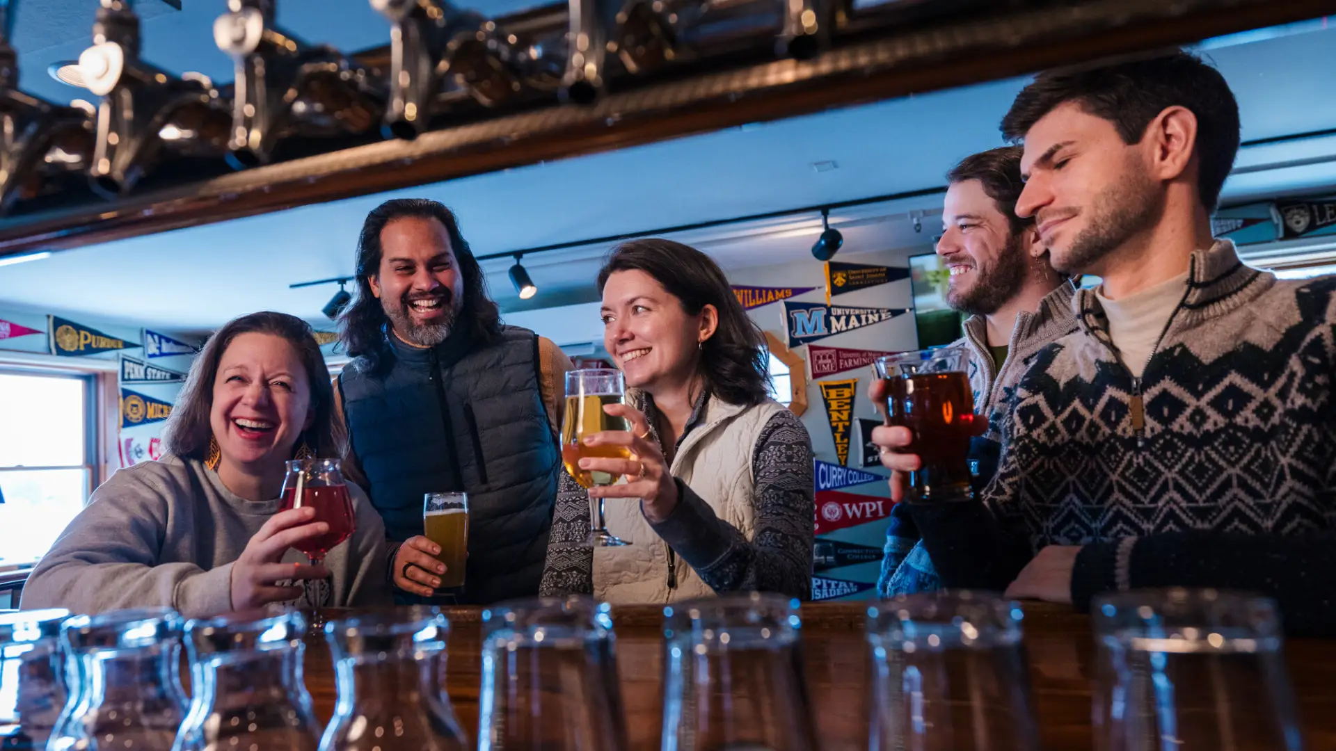 Group of friends seen between taps and beer glasses enjoying pints of beer and laughing