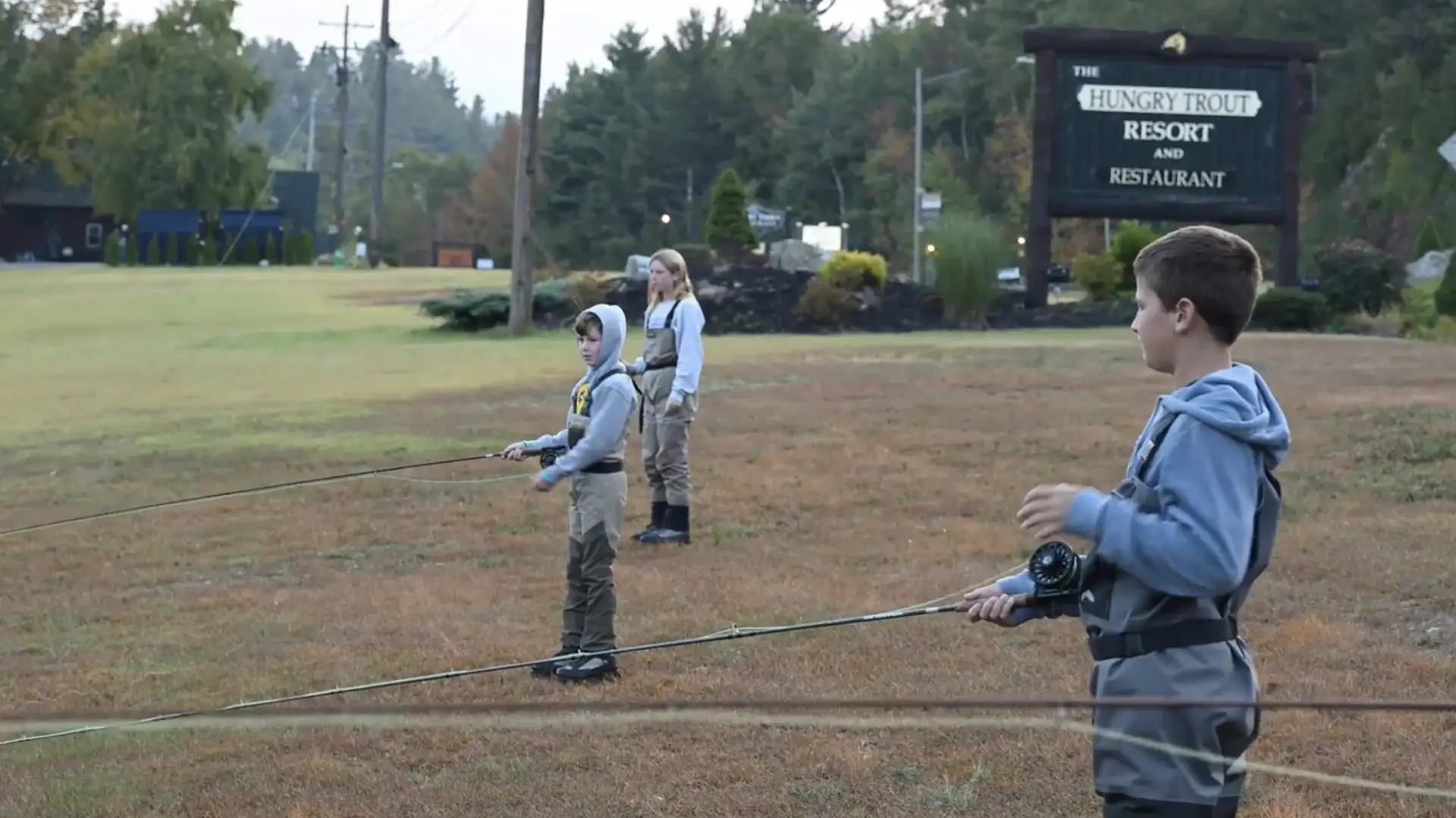 Three kids practice casting fishing rods on lawn
