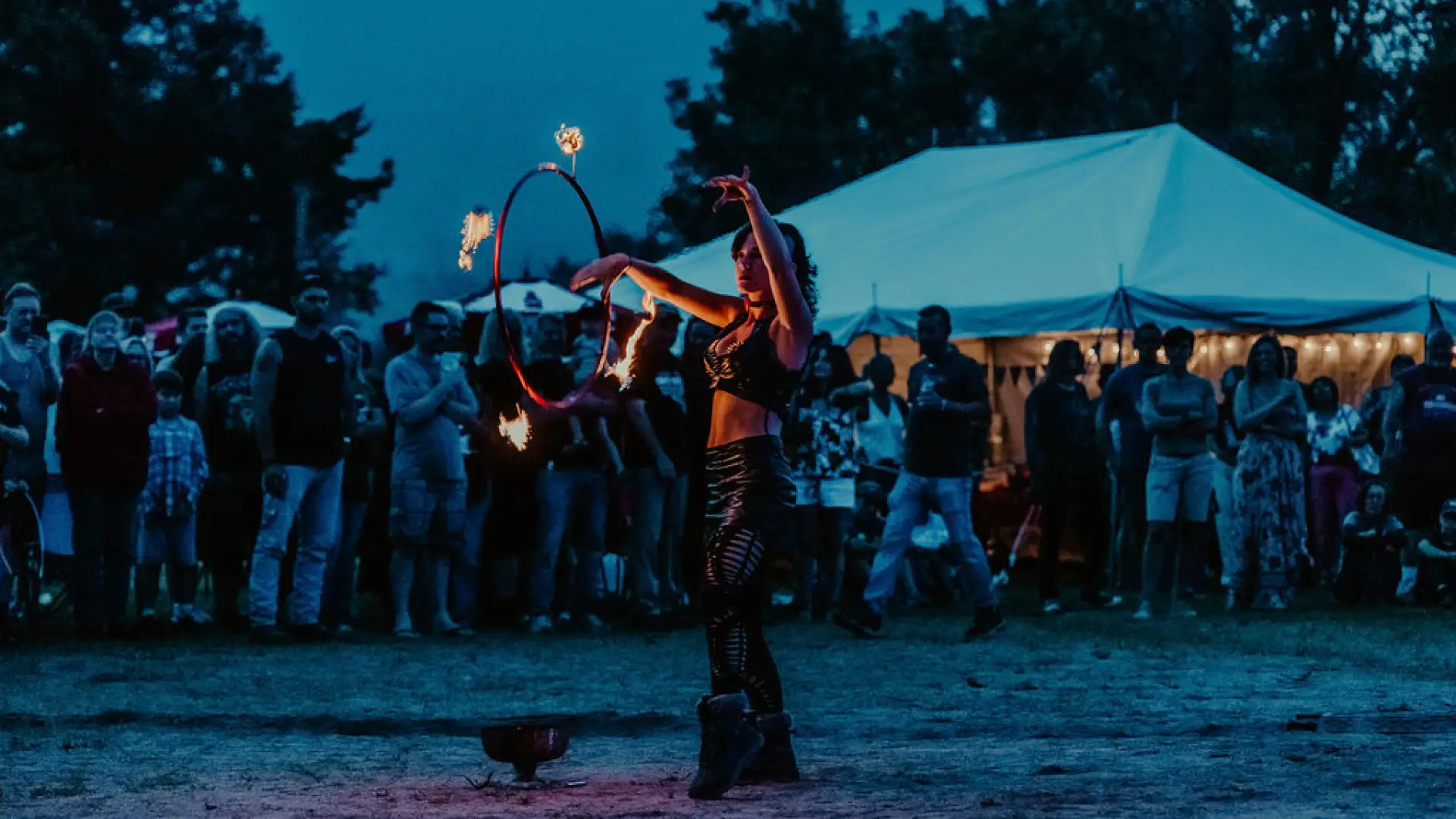 Fire dancer seen twirling flaming batons at music festival at dusk
