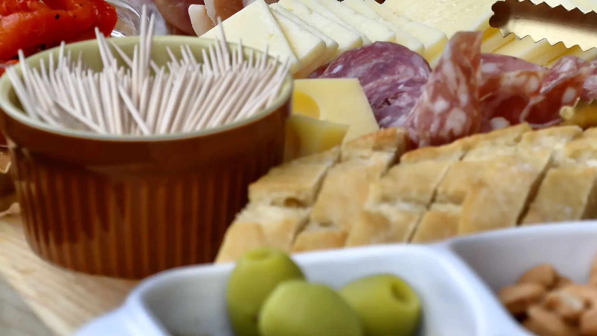 Meat and cheese charcuterie board with bread, peppers, toothpicks, and other accoutrement 