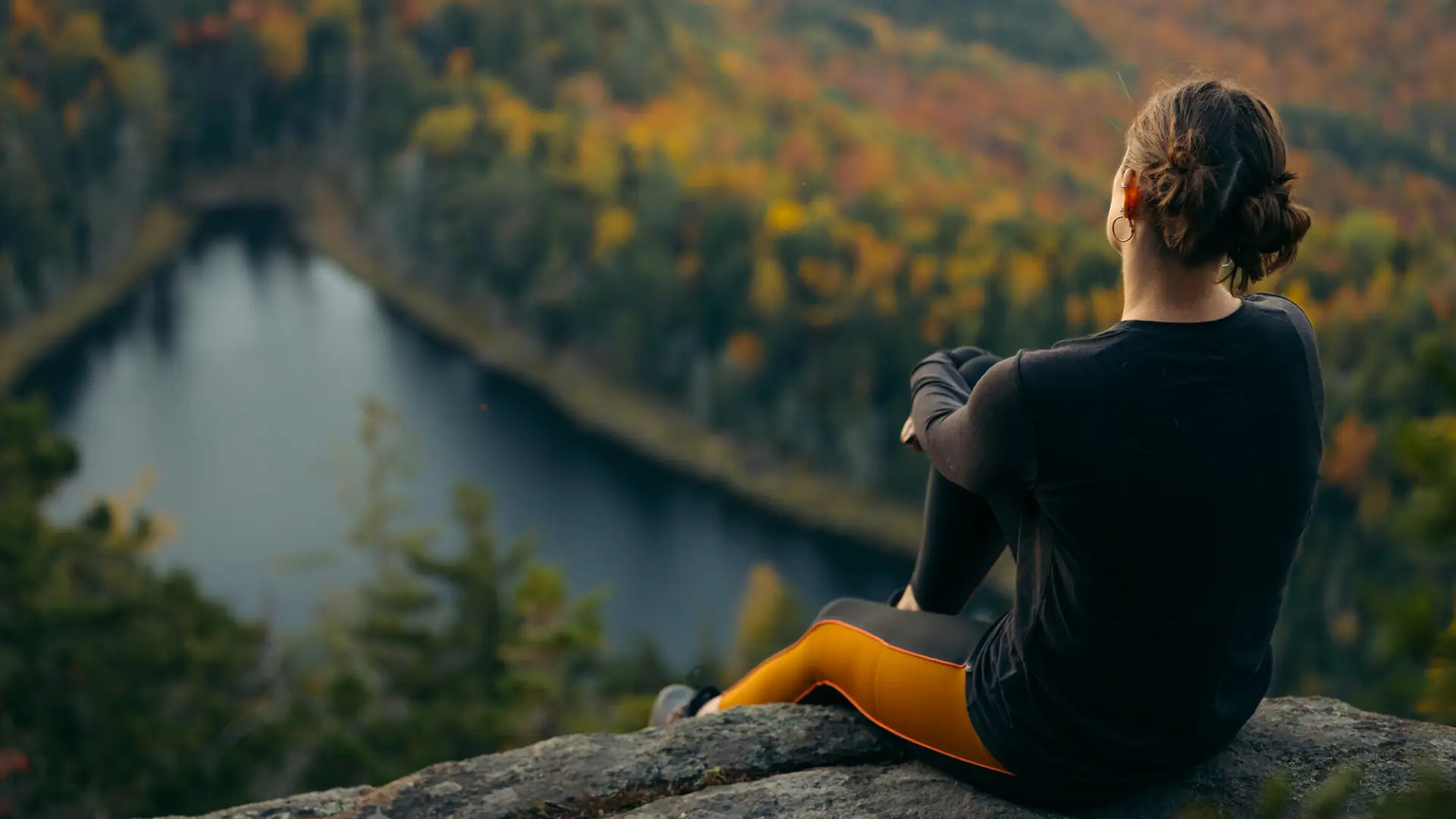 A woman sits on a rock overlooking fall foliage mountain views.