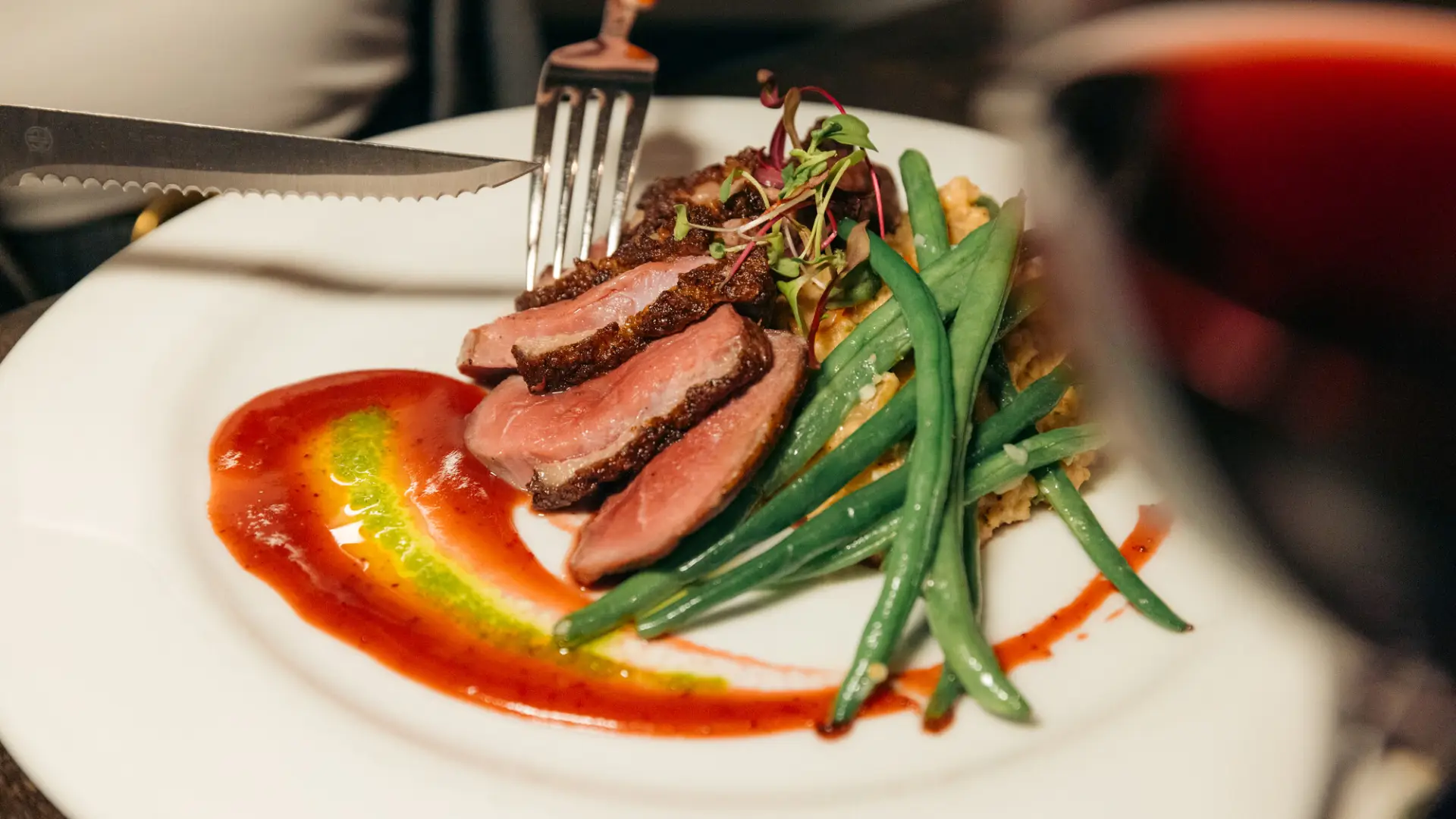 Fork and knife cutting into meat, quinoa, and green bean dish