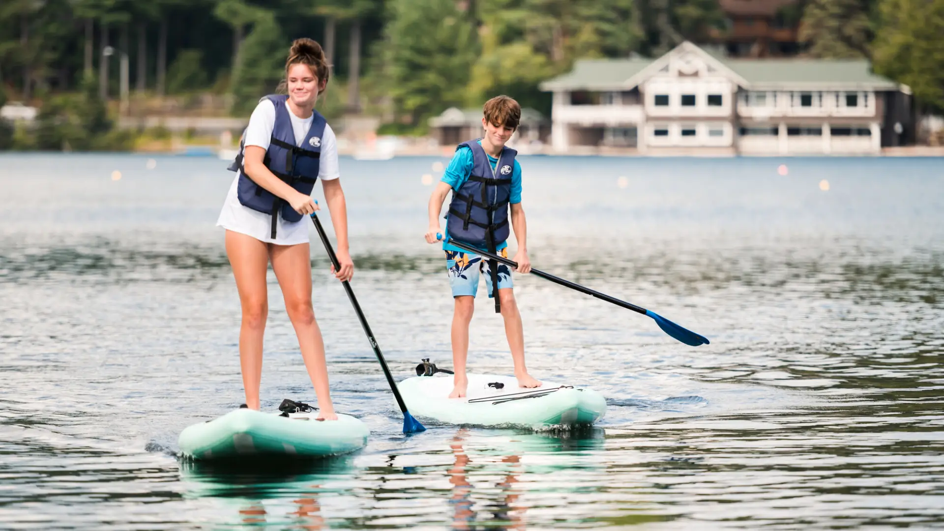 Two kids paddle on SUPs on Lake Placid.