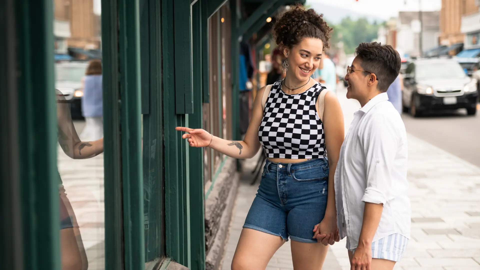 Two women hold hands and smile at a shop display on Lake Placid's quaint Main Street.