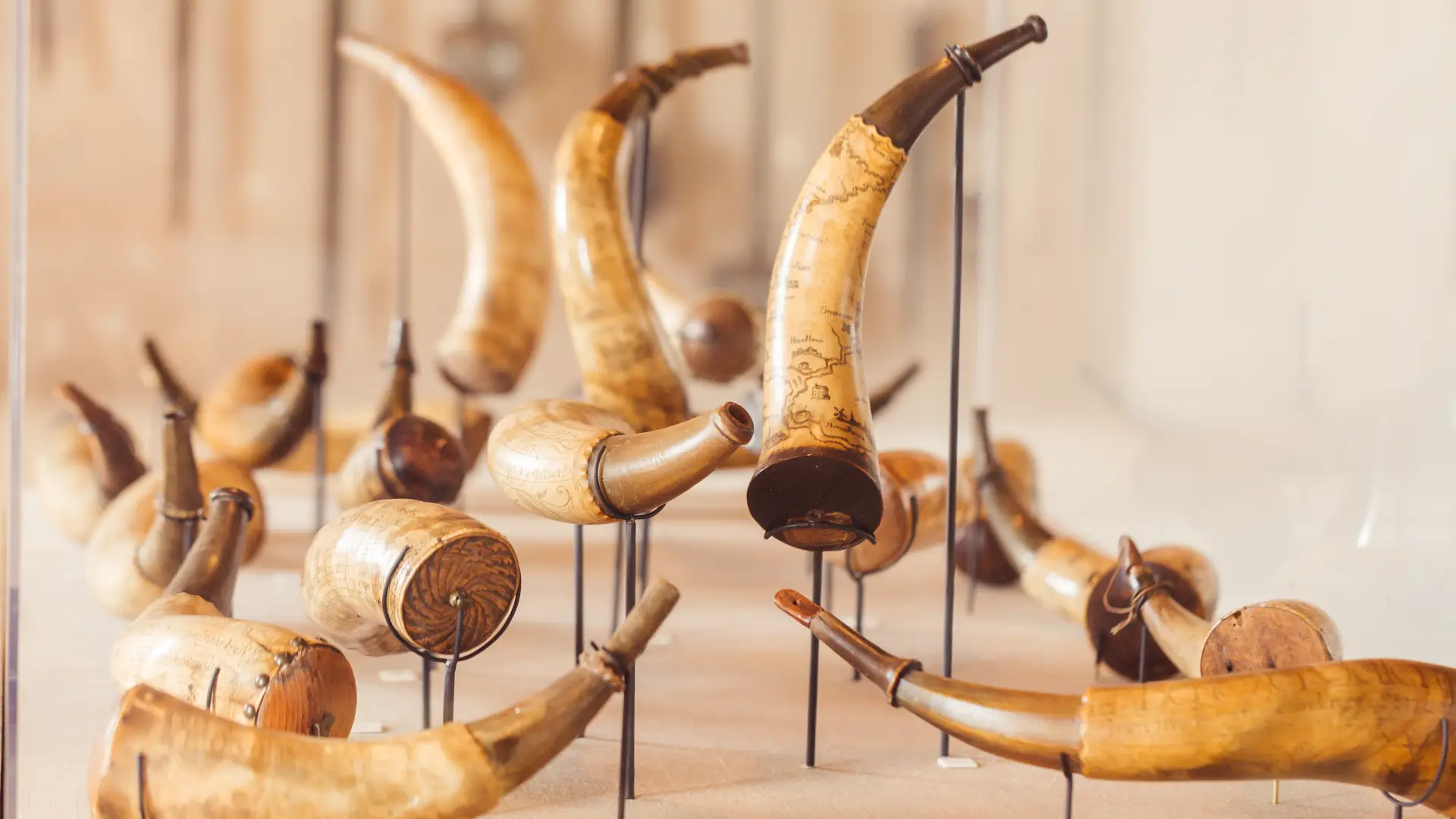 A collection of powder horns, some decorated with maps and adorned with metal dispensing tips.