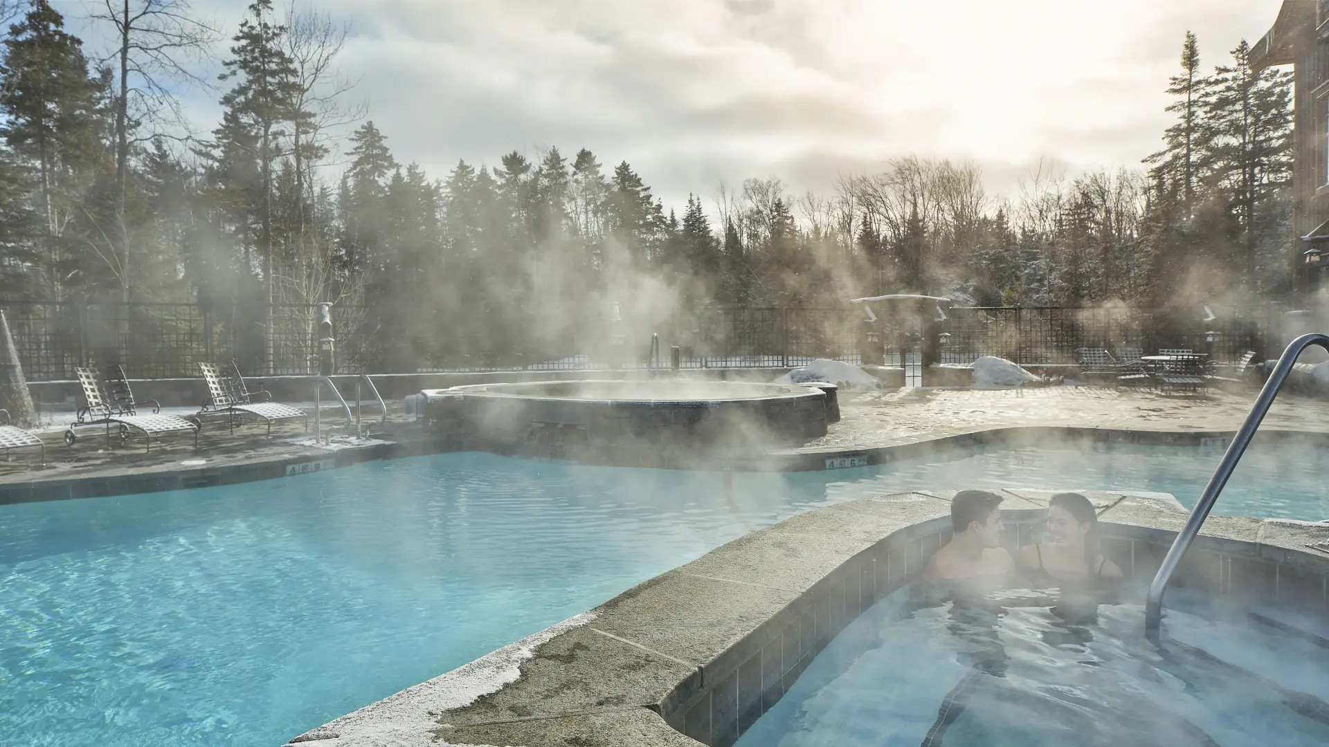 Two people sit in the water on a winter's day as steam rises from the outdoor swimming pool at the Whiteface Lodge