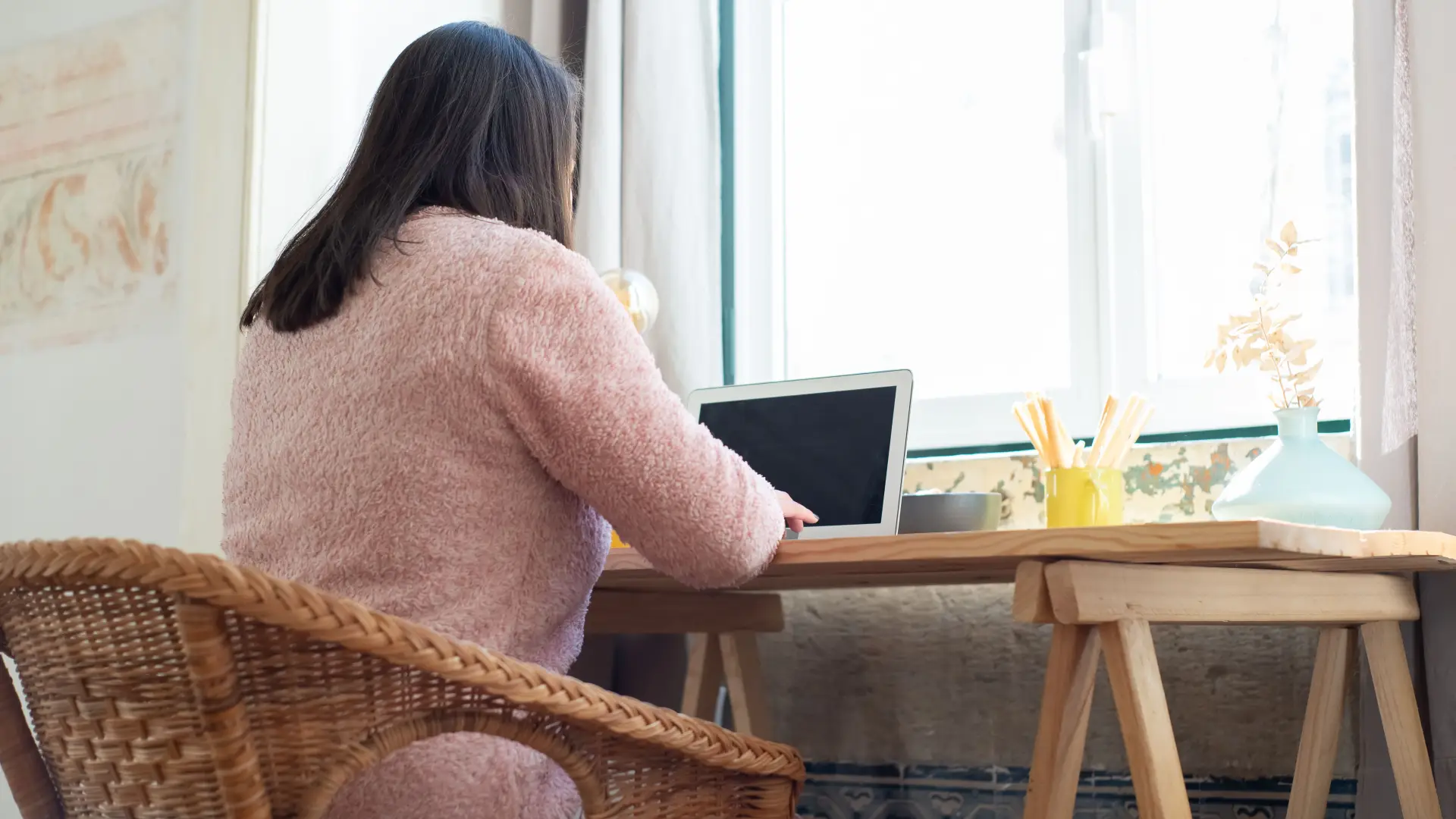 Stock image of a woman sitting at a desk turned away from the camera working on a laptop at home
