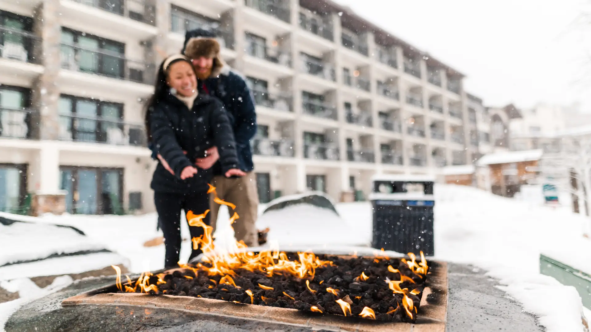 A couple standing in front of a fire during their stay in Lake Placid.