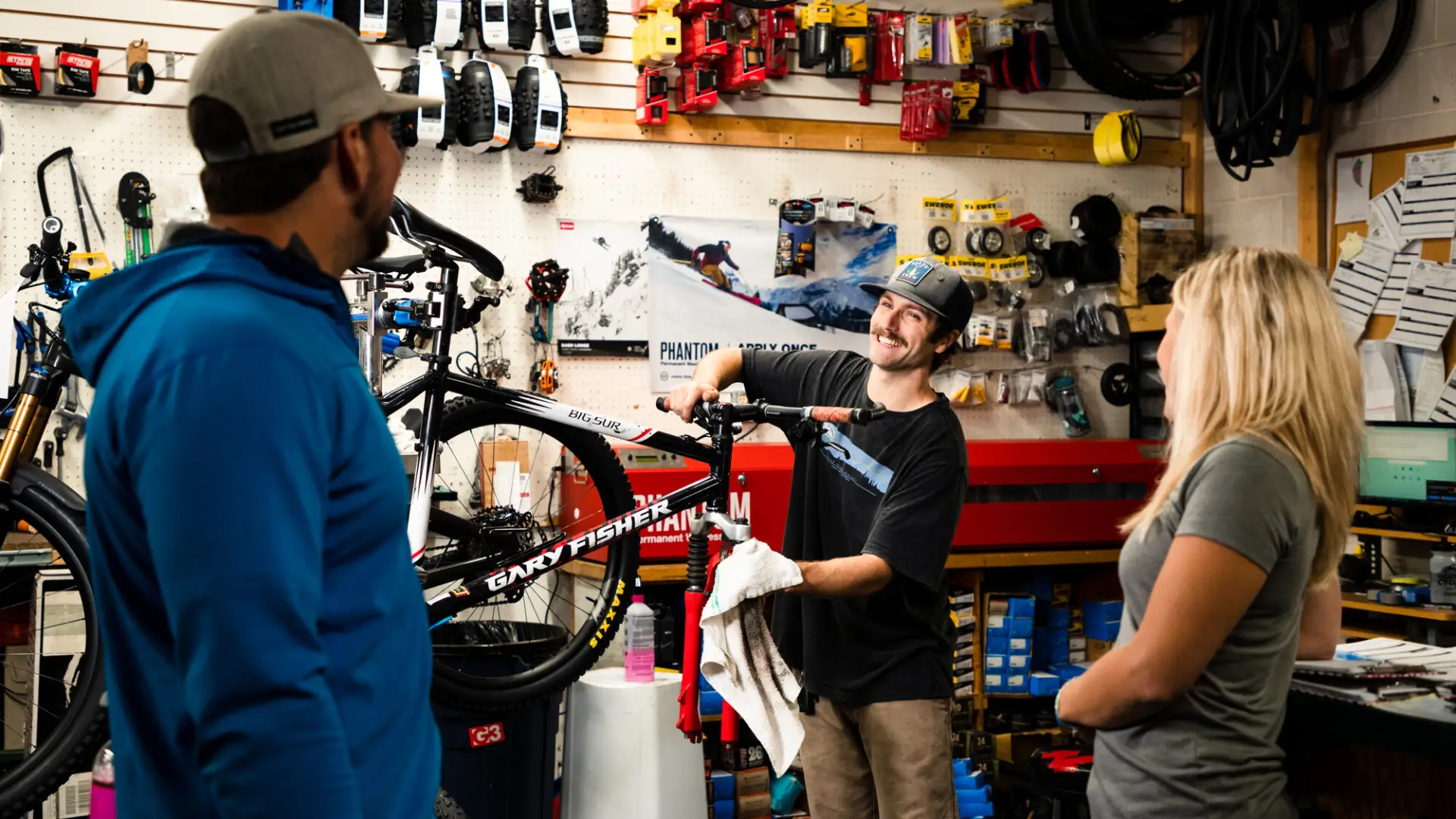 A man works on a bike while speaking to customers in a bike shop. 
