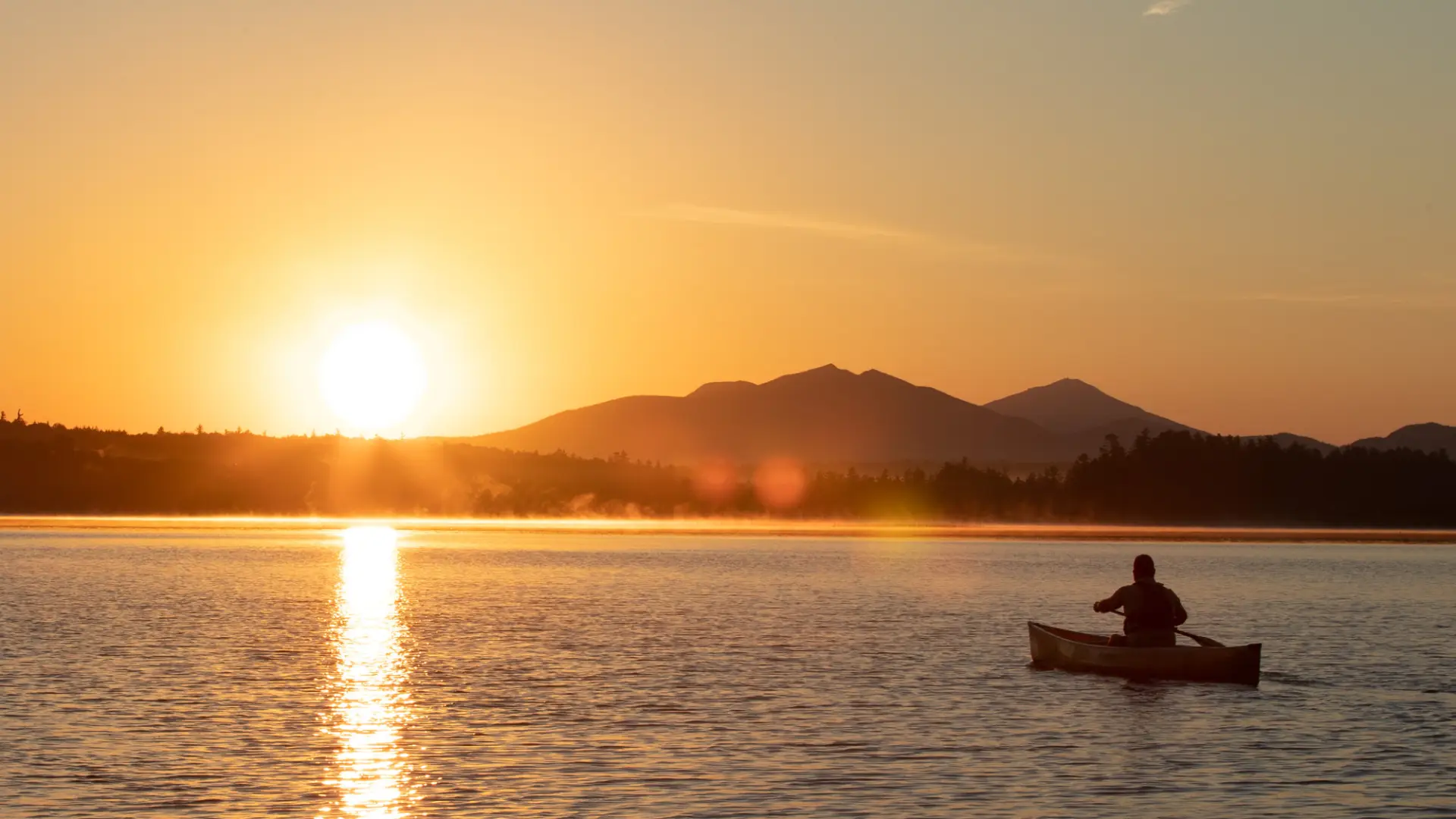A person canoeing on calm water during sunset.