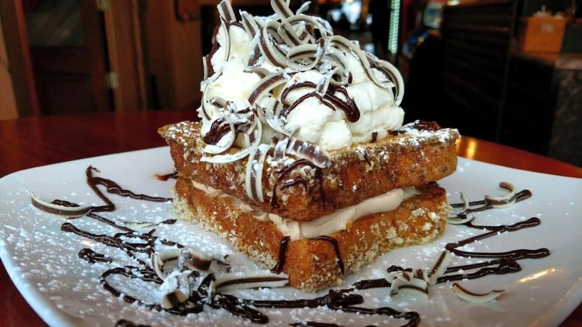 Two pieces of French toast with creamy filling and topped with a big mound of frosting and chocolate curls.