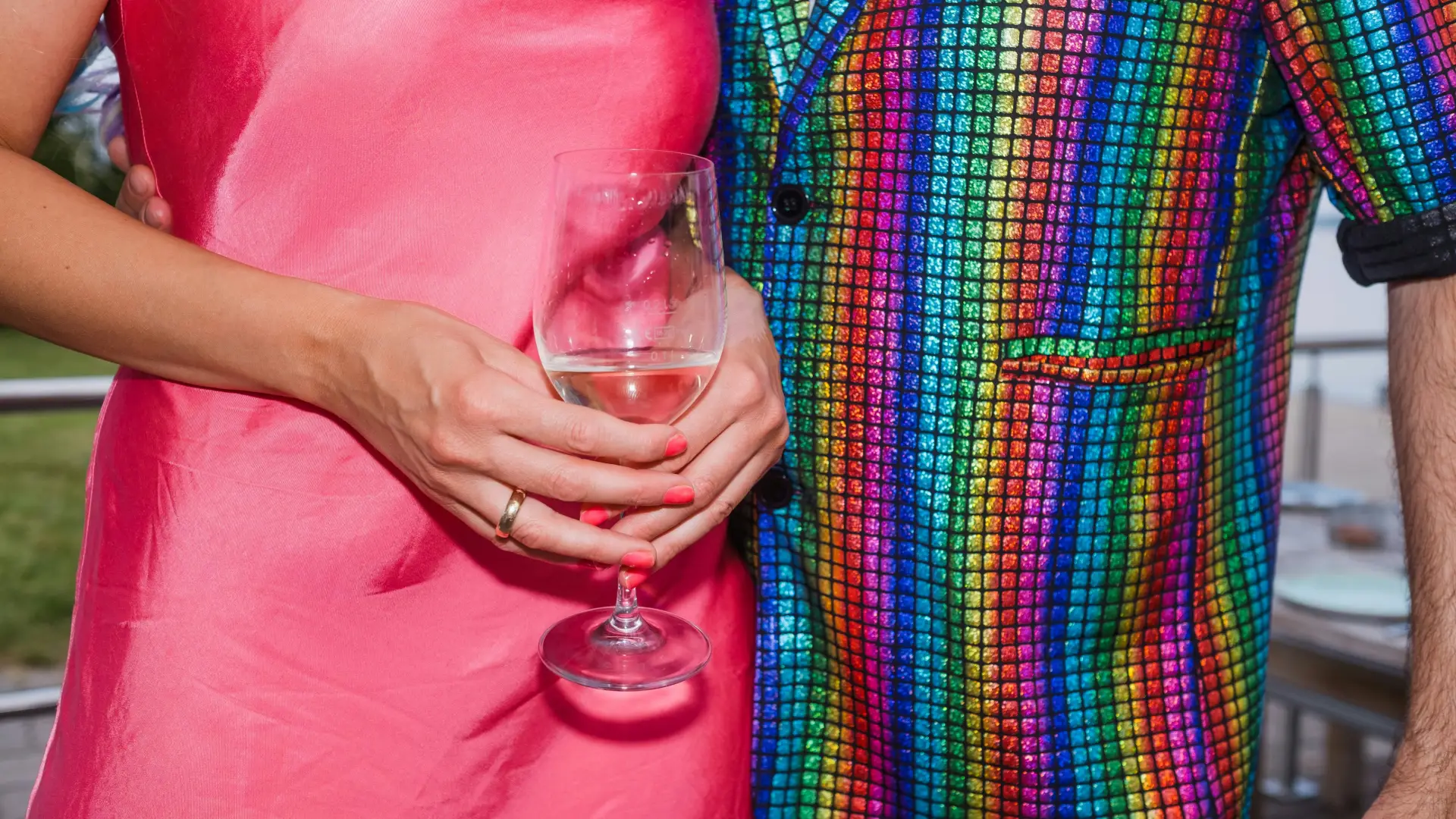 Stock image of person in pink dress holding glass of wine standing next to person in rainbow check shirt