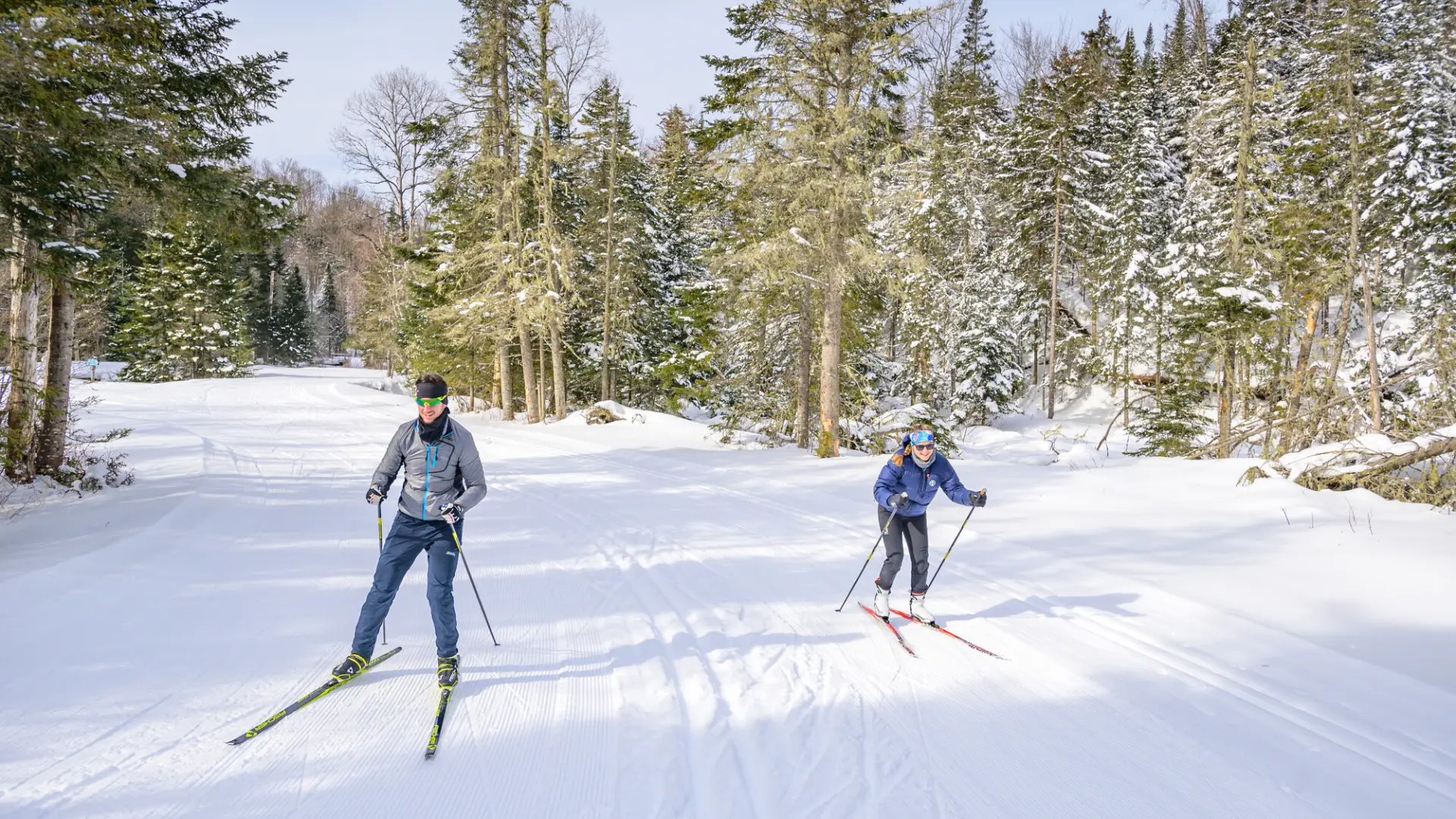 Two women cross-country ski on a wide open path in winter. 