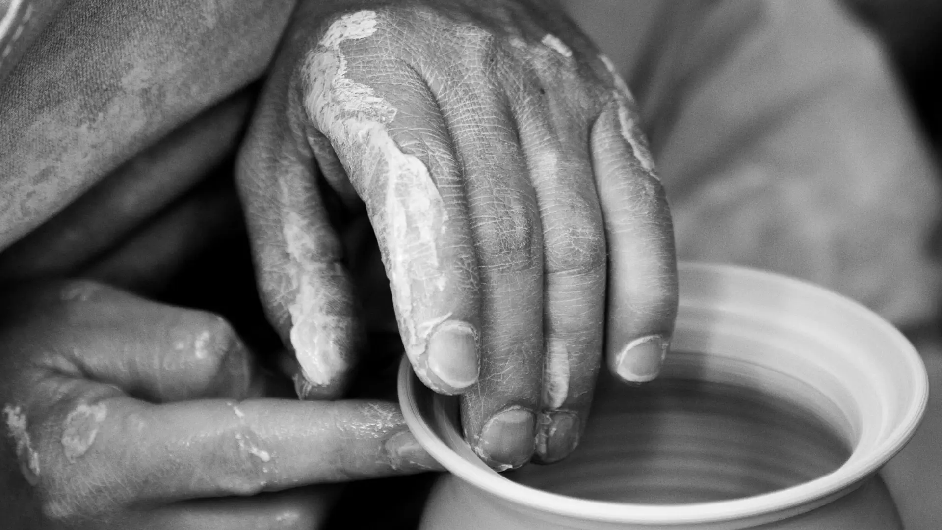 Black and white stock image of hands shaping clay pot with wet clay on hands