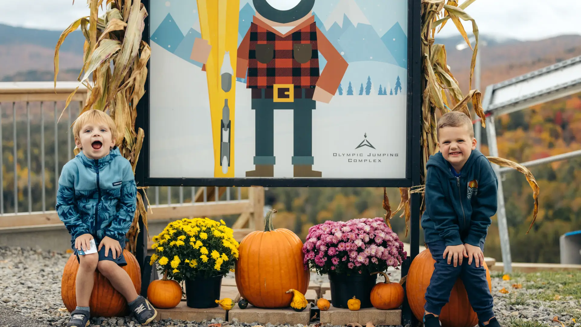 Two kids sitting next to pumpkins at a Lake Placid event.