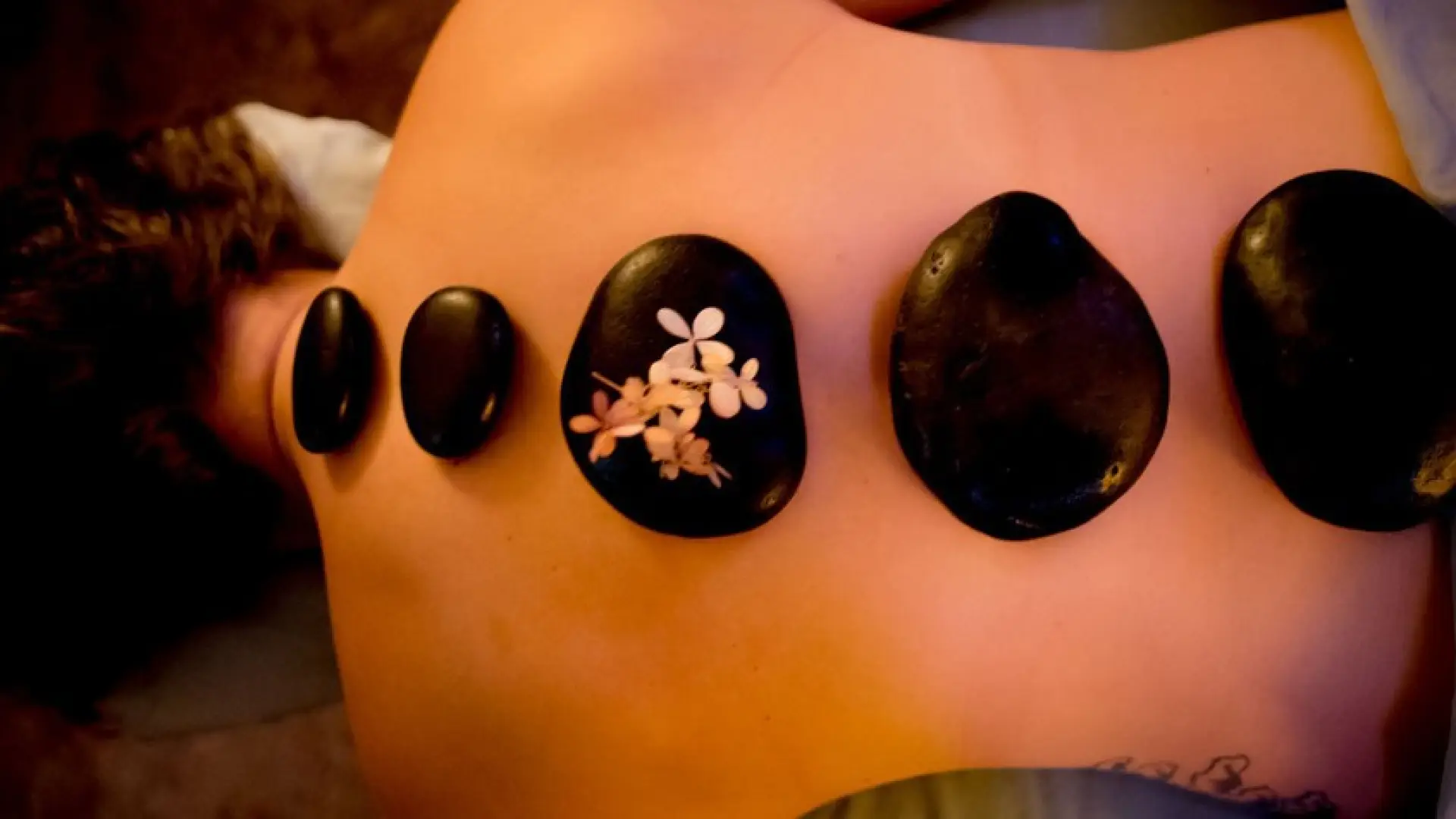 Hot stone massage tools are laid upon the spine of a person